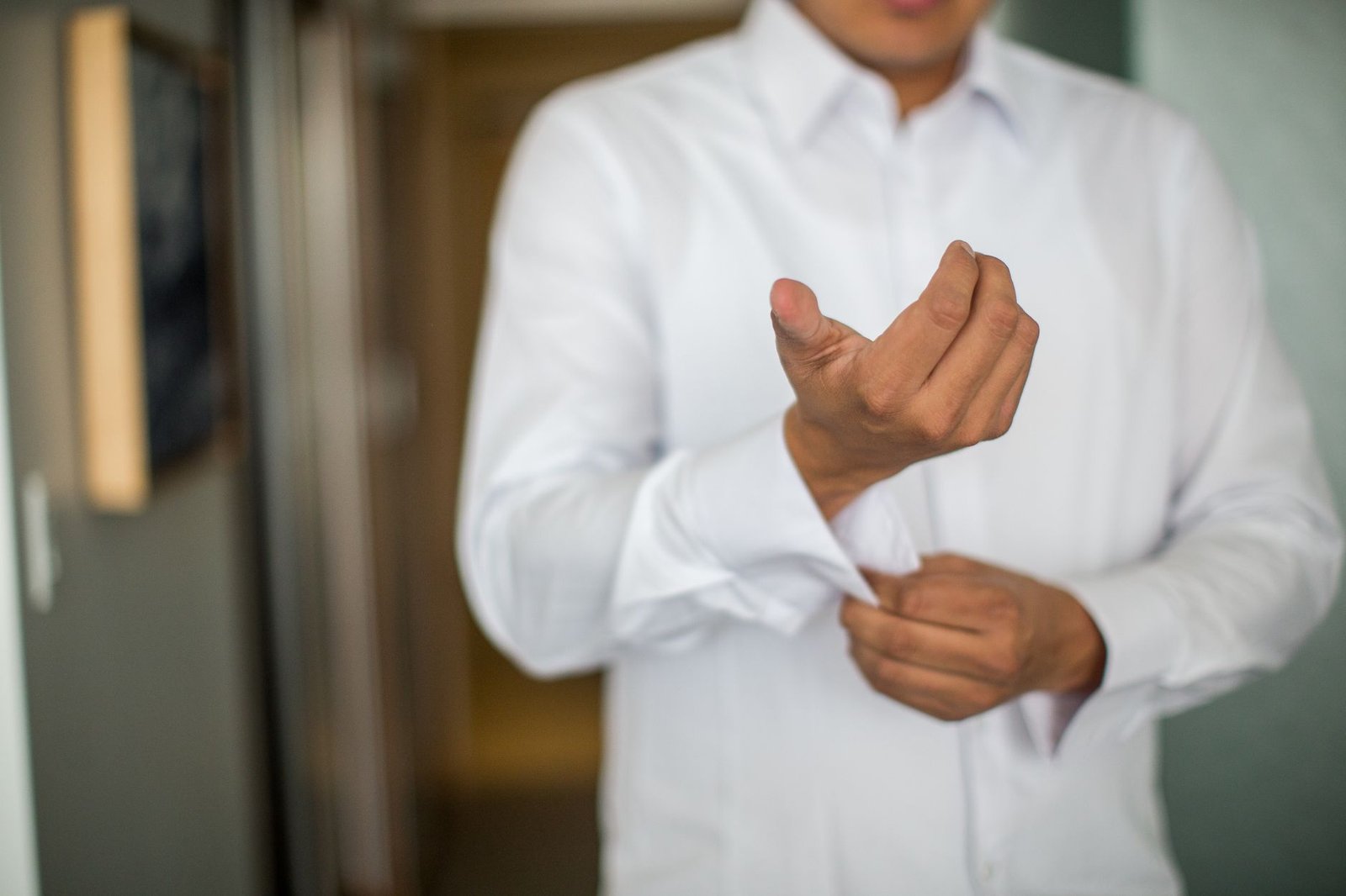 Close-up of a man adjusting his shirt cuffs, focusing on a white long-sleeve shirt indoors.