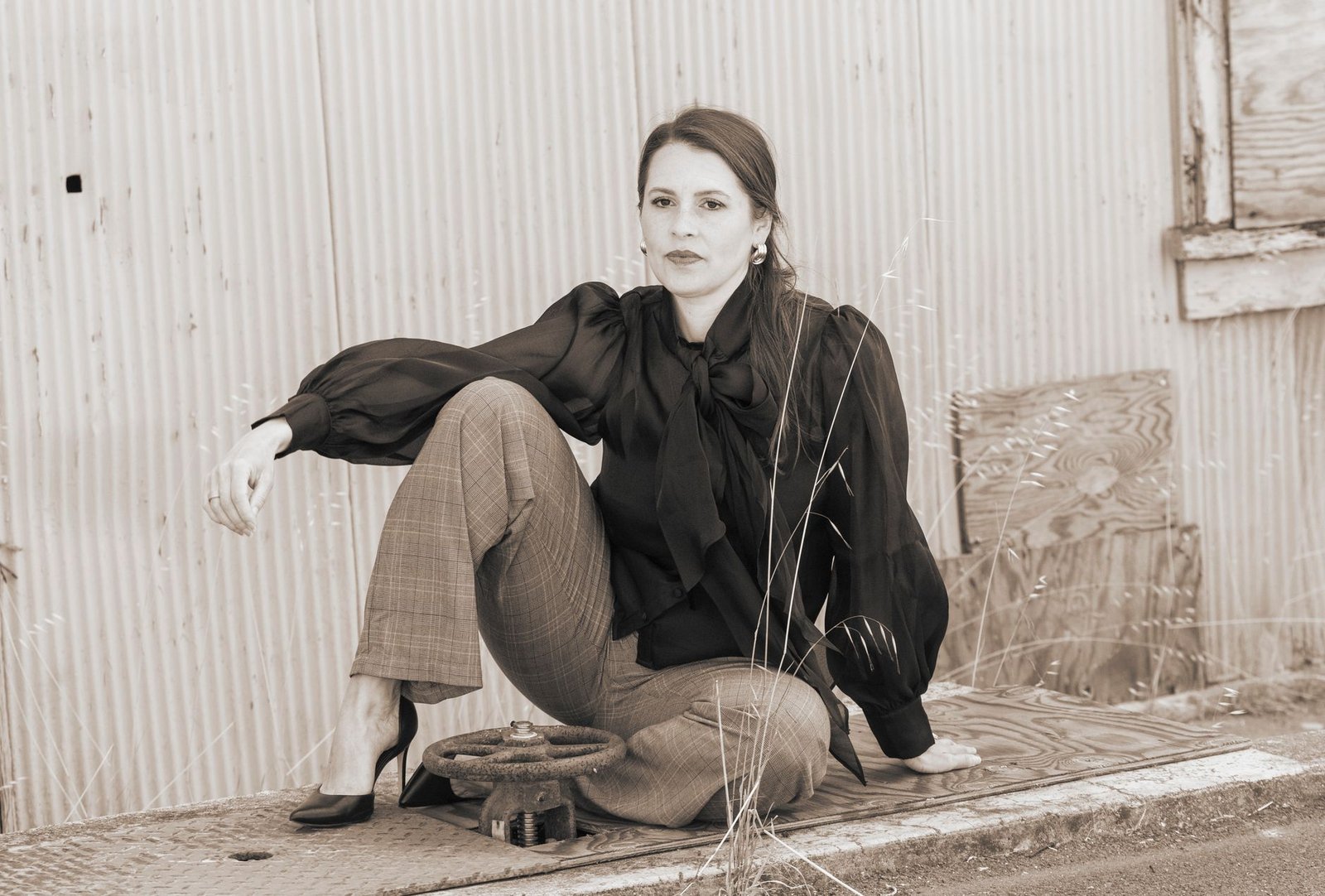 Sepia-toned portrait of a woman in vintage clothing sitting on a rustic surface outdoors.