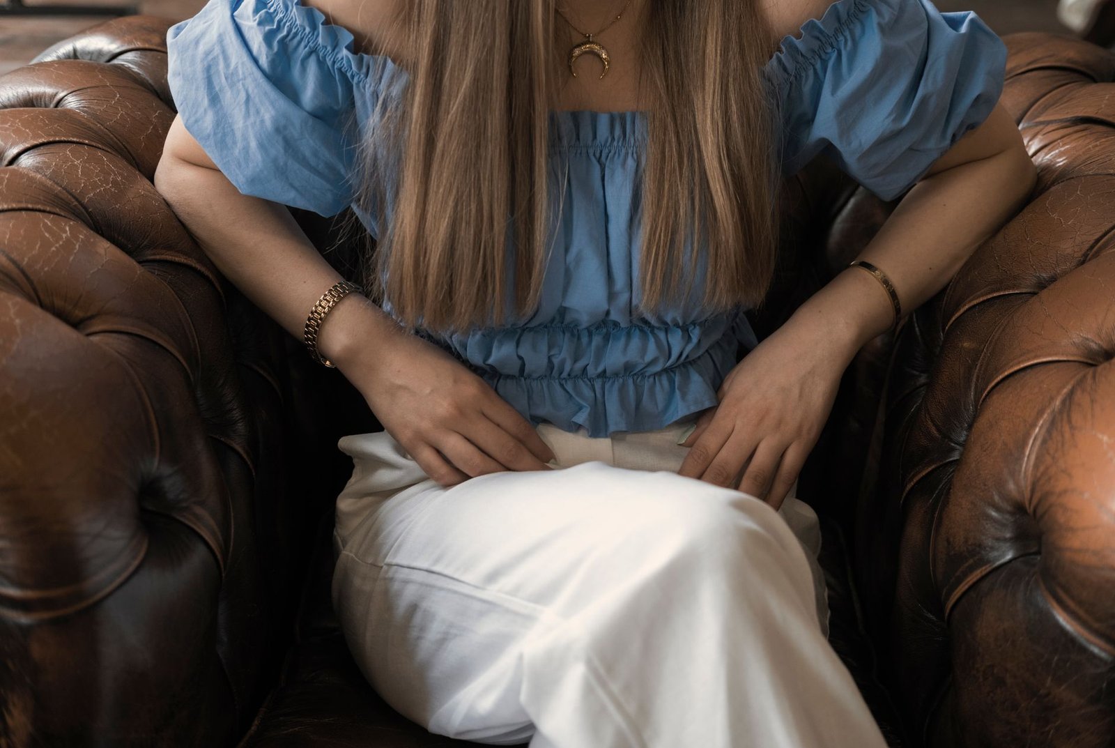 Crop unrecognizable young female in casual clothes resting in comfortable leather brown armchair with legs crossed and leaning on elbows