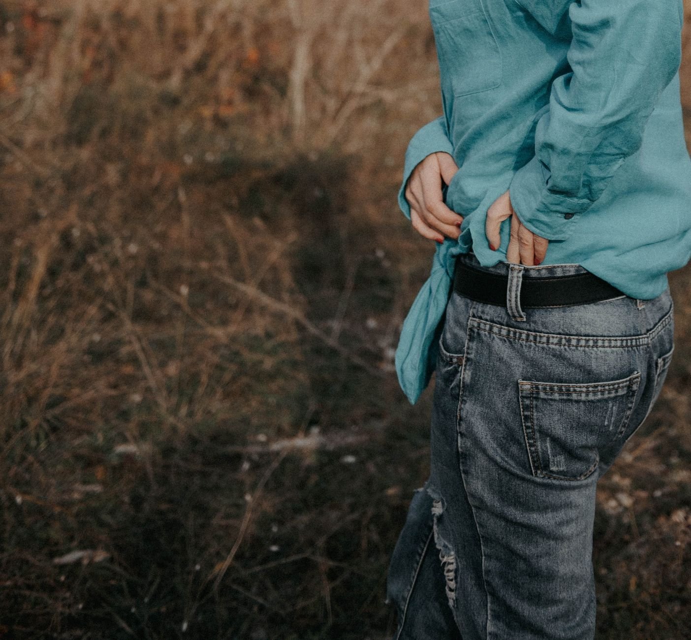 Close-up of a person in denim jeans and turquoise top in an autumn field.