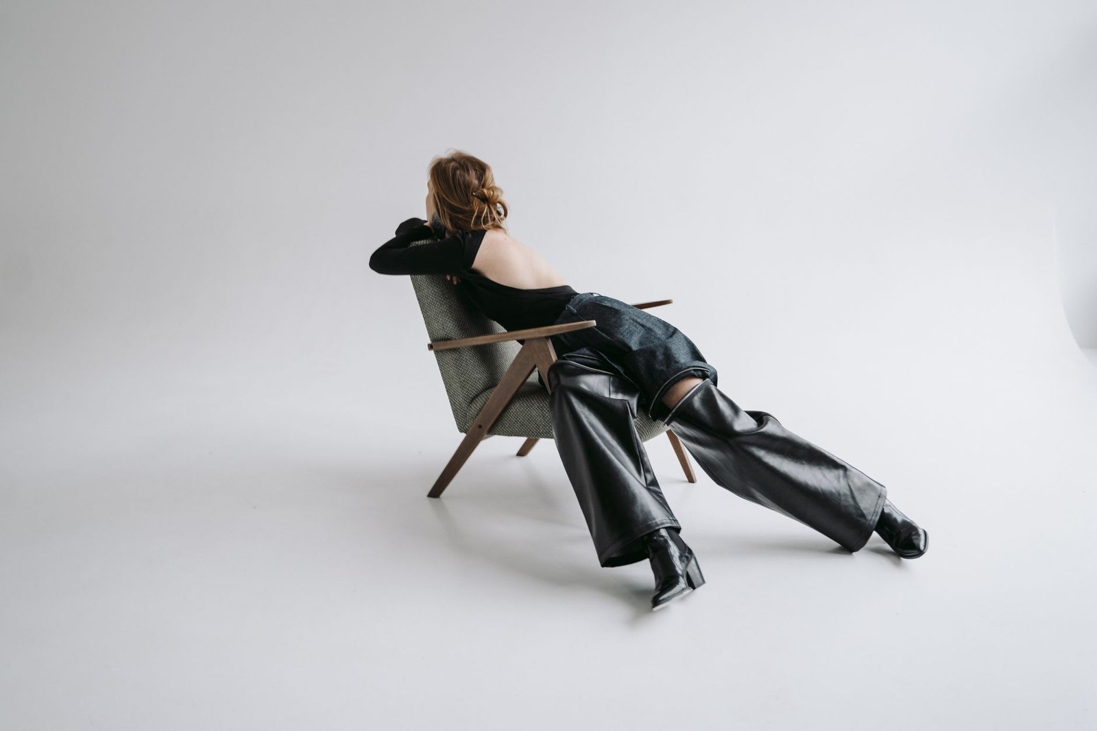 Stylish woman in leather pants relaxing on chair in minimalist studio setting.