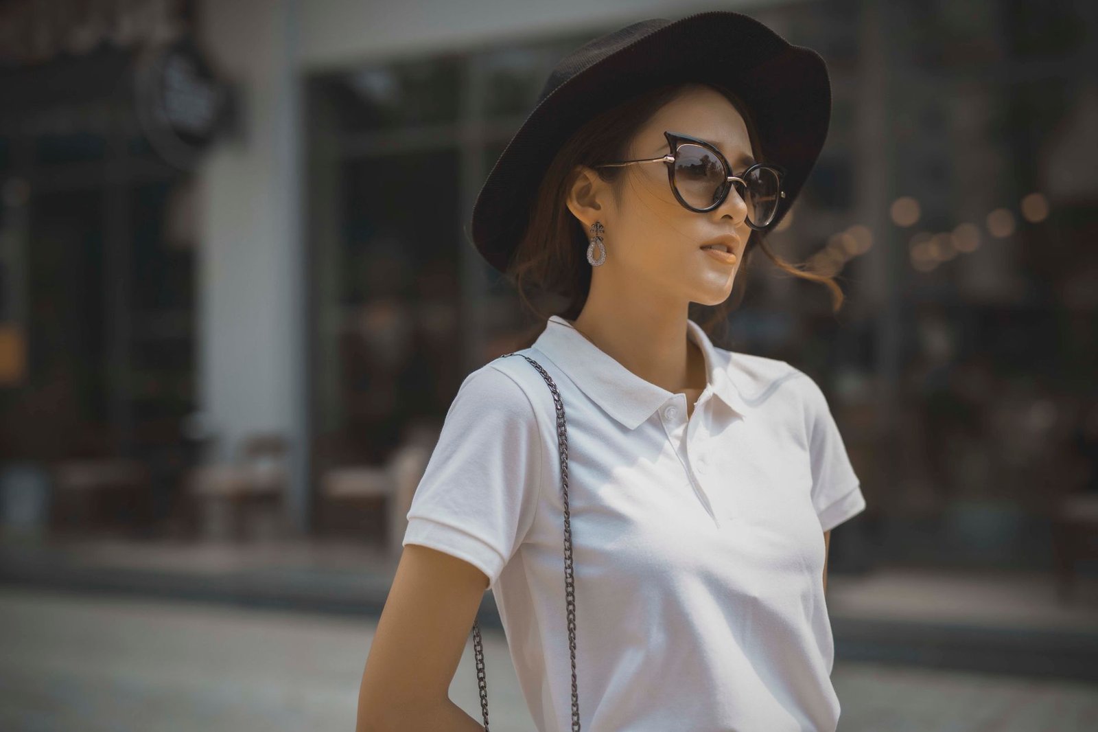 Fashionable woman in a white polo shirt, sunglasses, and black hat outdoors, exuding style and confidence.