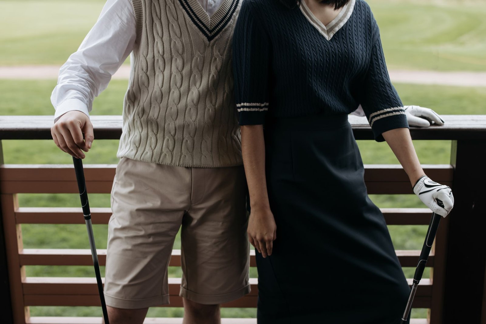 Elegant golfers in fashionable preppy attire holding clubs on the golf course.