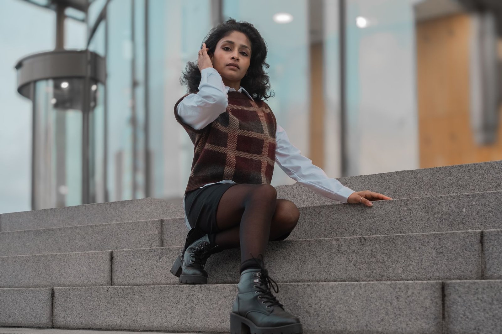 A fashionable young girl poses confidently on modern outd or steps in urban setting.
