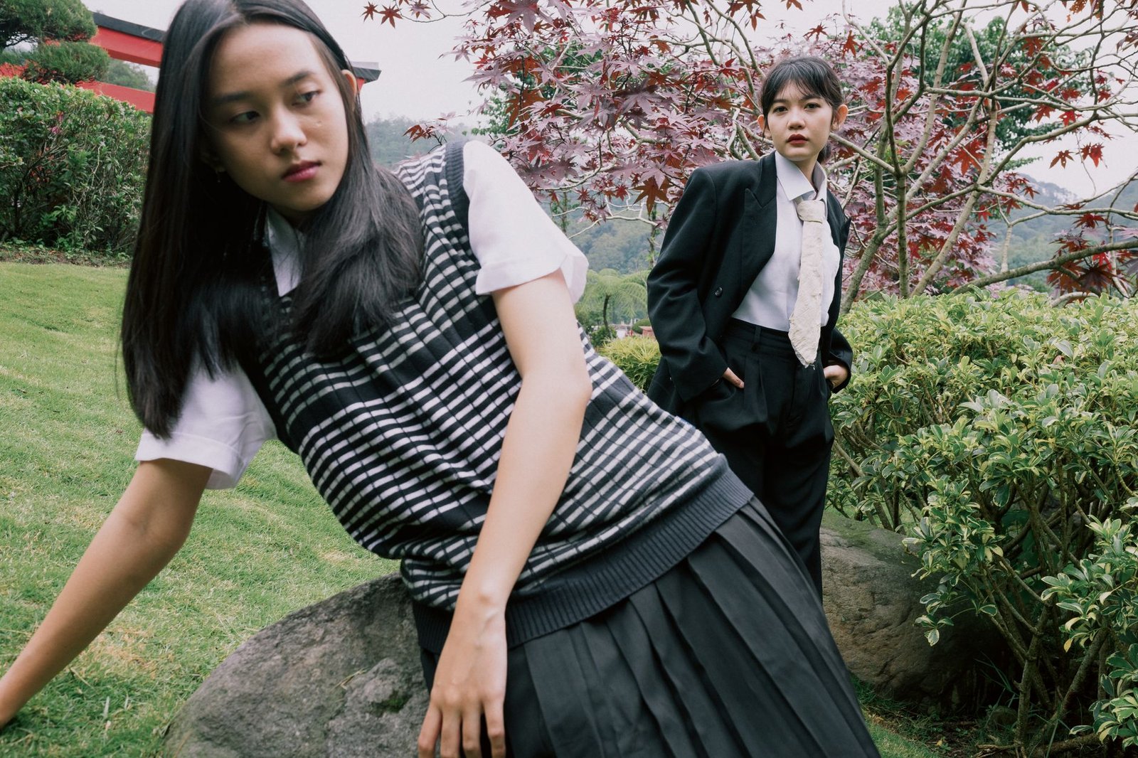 Two stylish young women pose in a serene garden, showcasing fashion and nature.