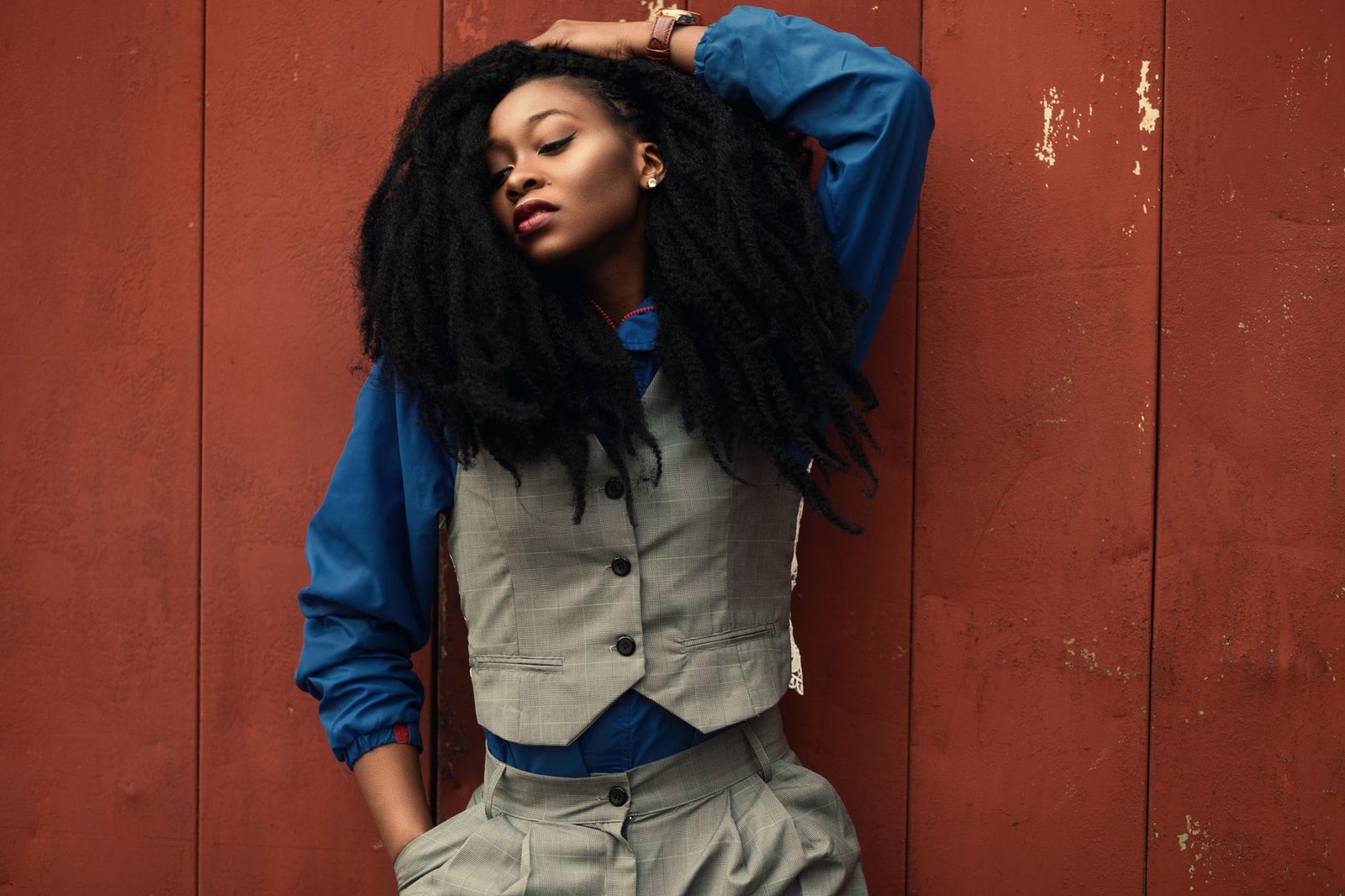 A fashionable woman poses with a confident look against a rustic red wall.