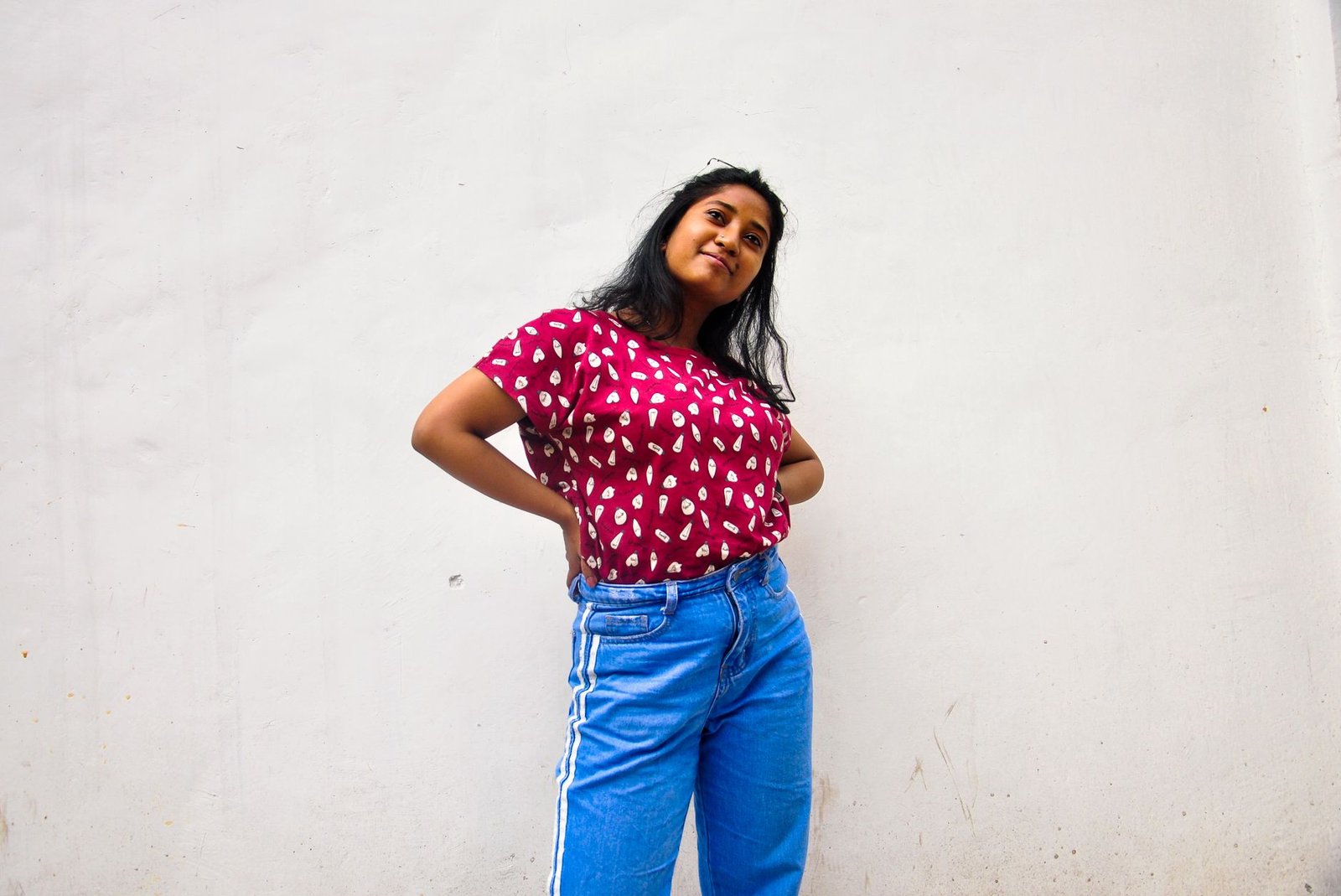 A confident woman in a stylish outfit posing against a plain wall exuding casual beauty and charm.