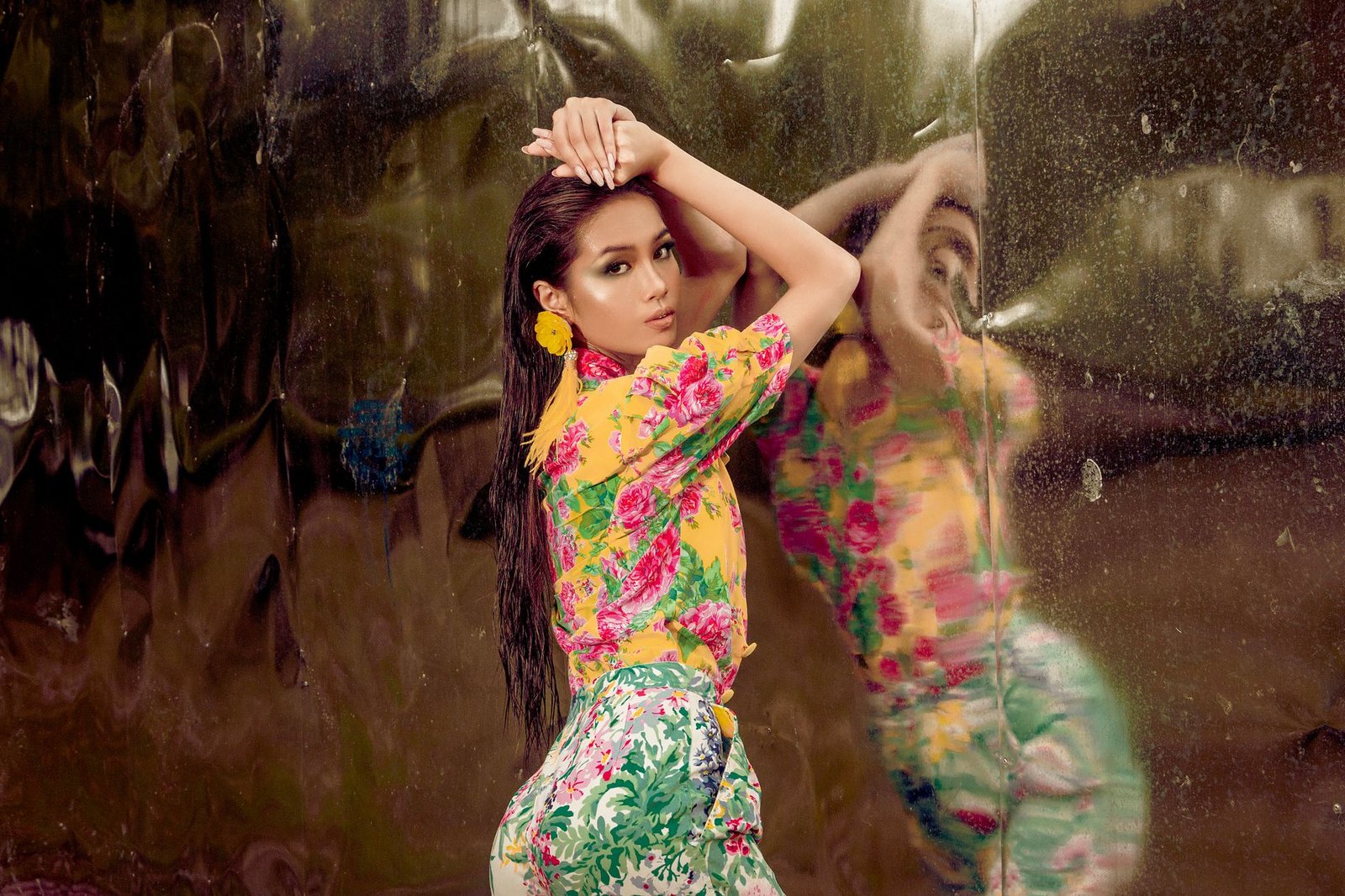 Stylish model in colorful floral attire posing against a reflective wall in a studio setting.