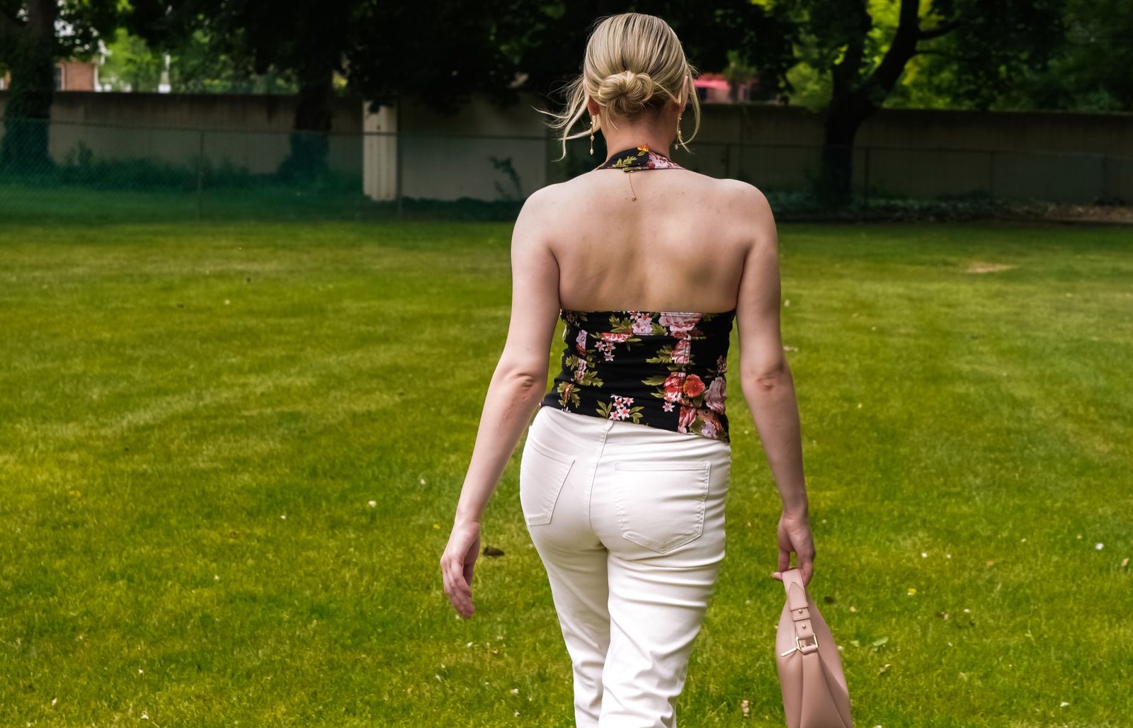 Rear view of a woman in a floral top and white pants walking outdoors on a sunny day.