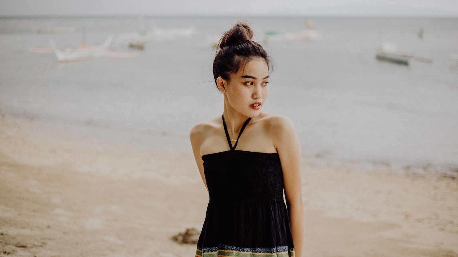 Elegant woman in a halter top on a serene Philippine each with boats in the background.