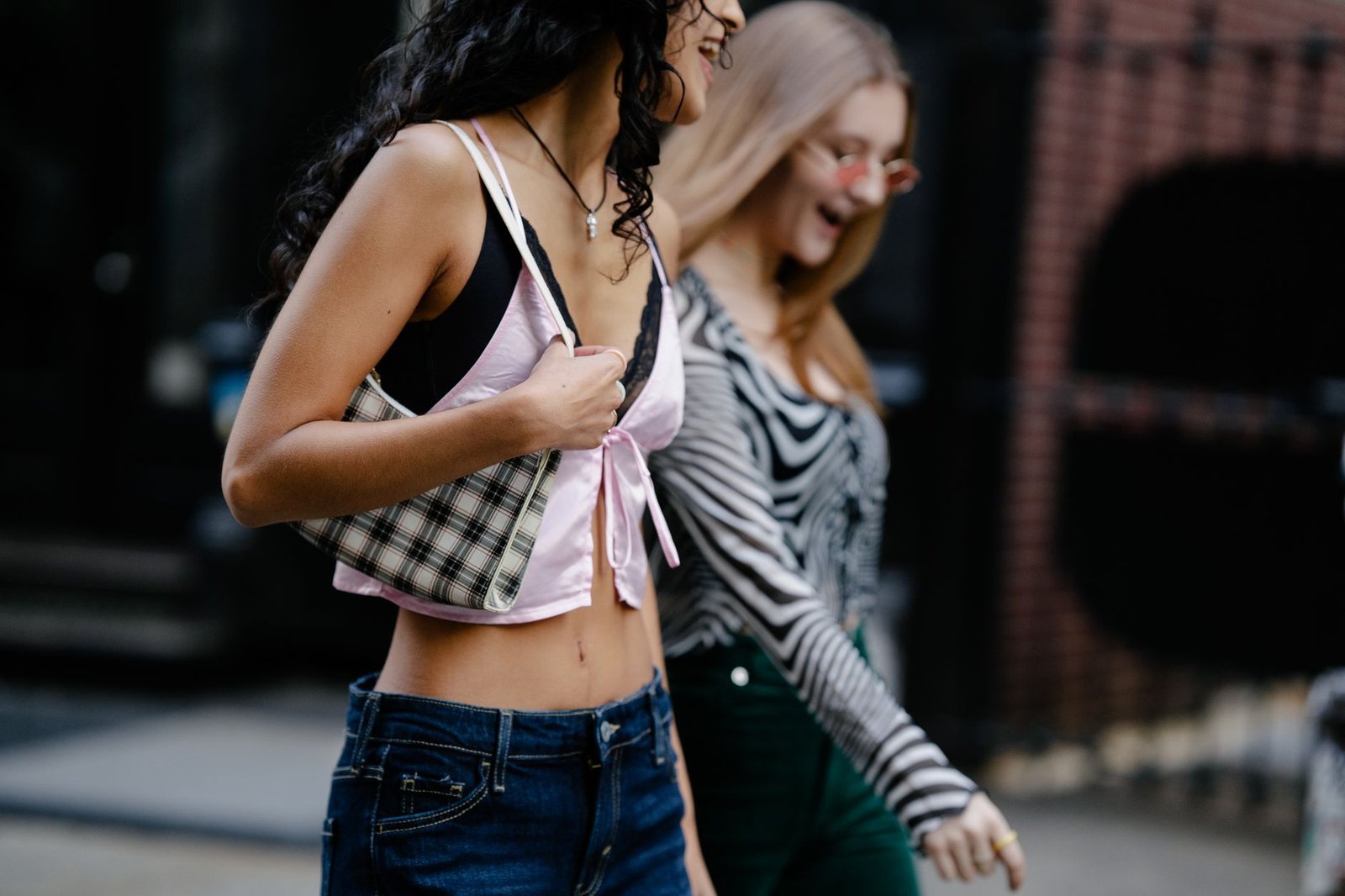 Two fashionable women walking and chatting in an urban area, showcasing street style.