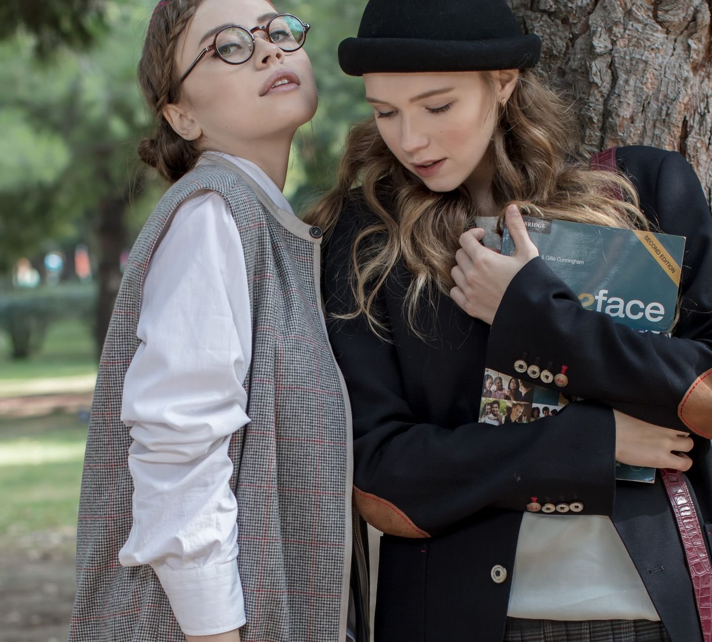 Two young women in fashionable attire holding a book in an outdoor setting.