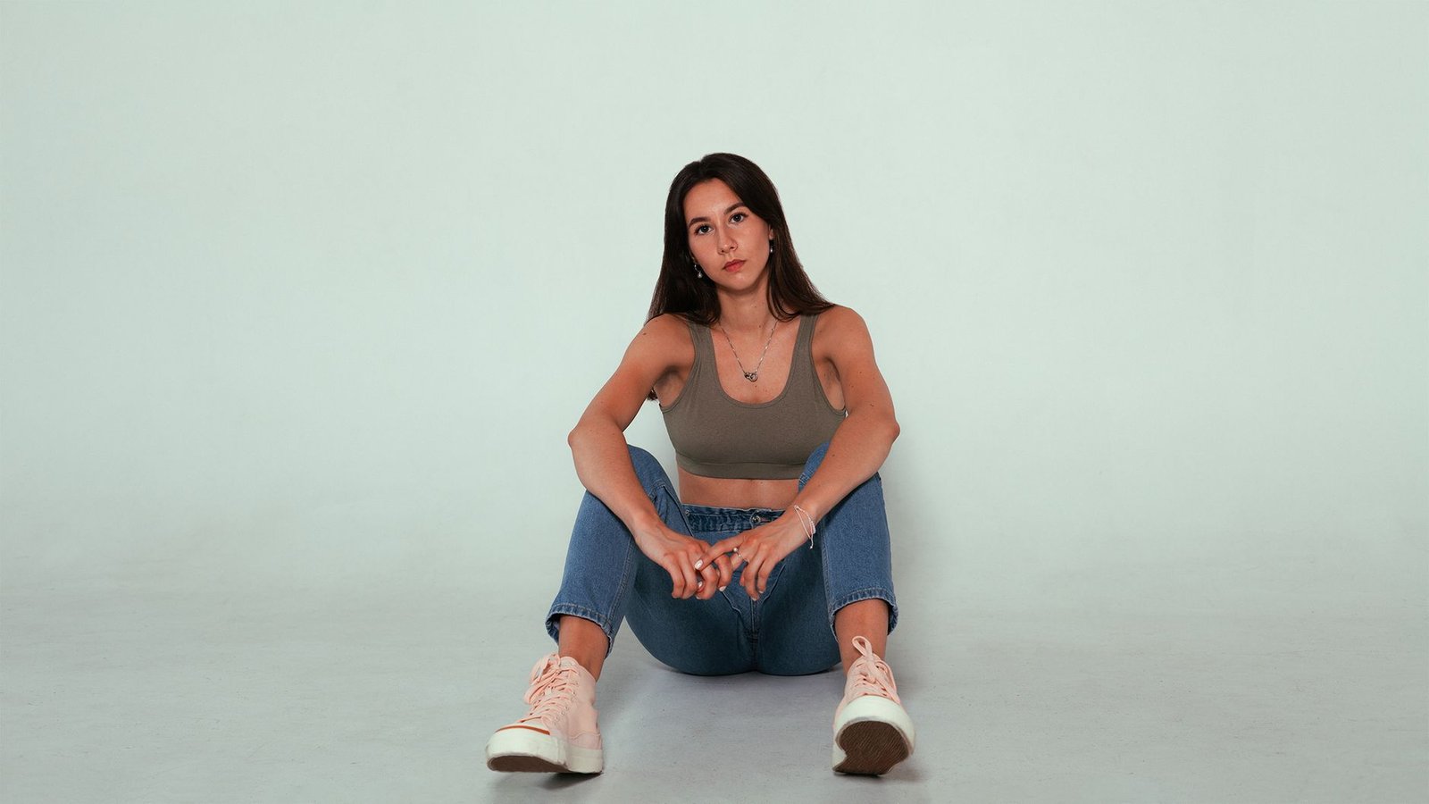 Portrait of a young woman in a casual outfit sitting against a neutral background. Studio shoot.