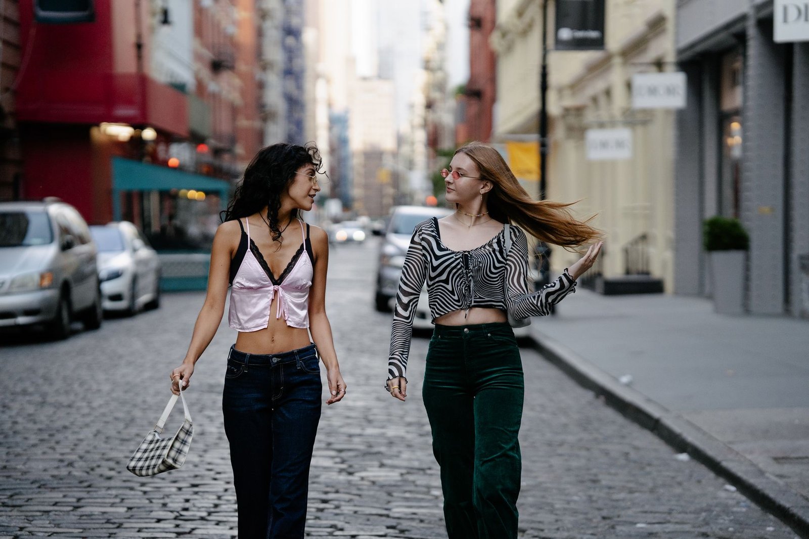 Two fashionable young women walking on a city street, showcasing trendy outfits and style.