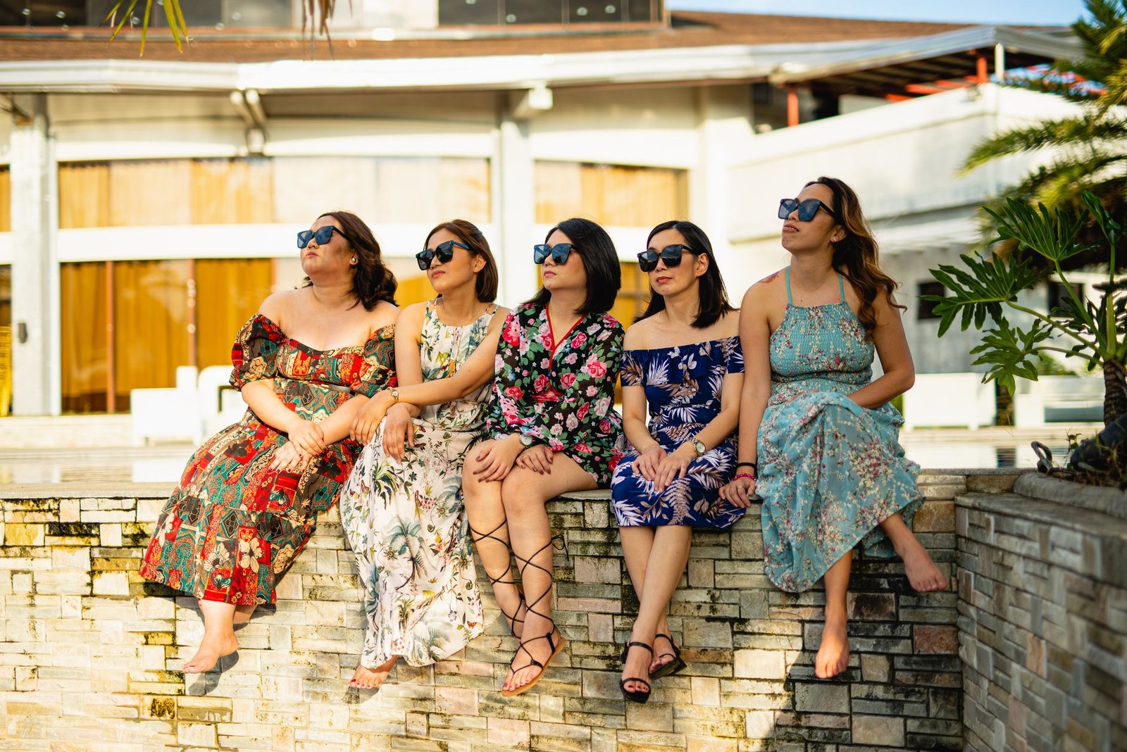 Five stylish women in sundresses and sunglasses enjoying a sunny day by the pool.