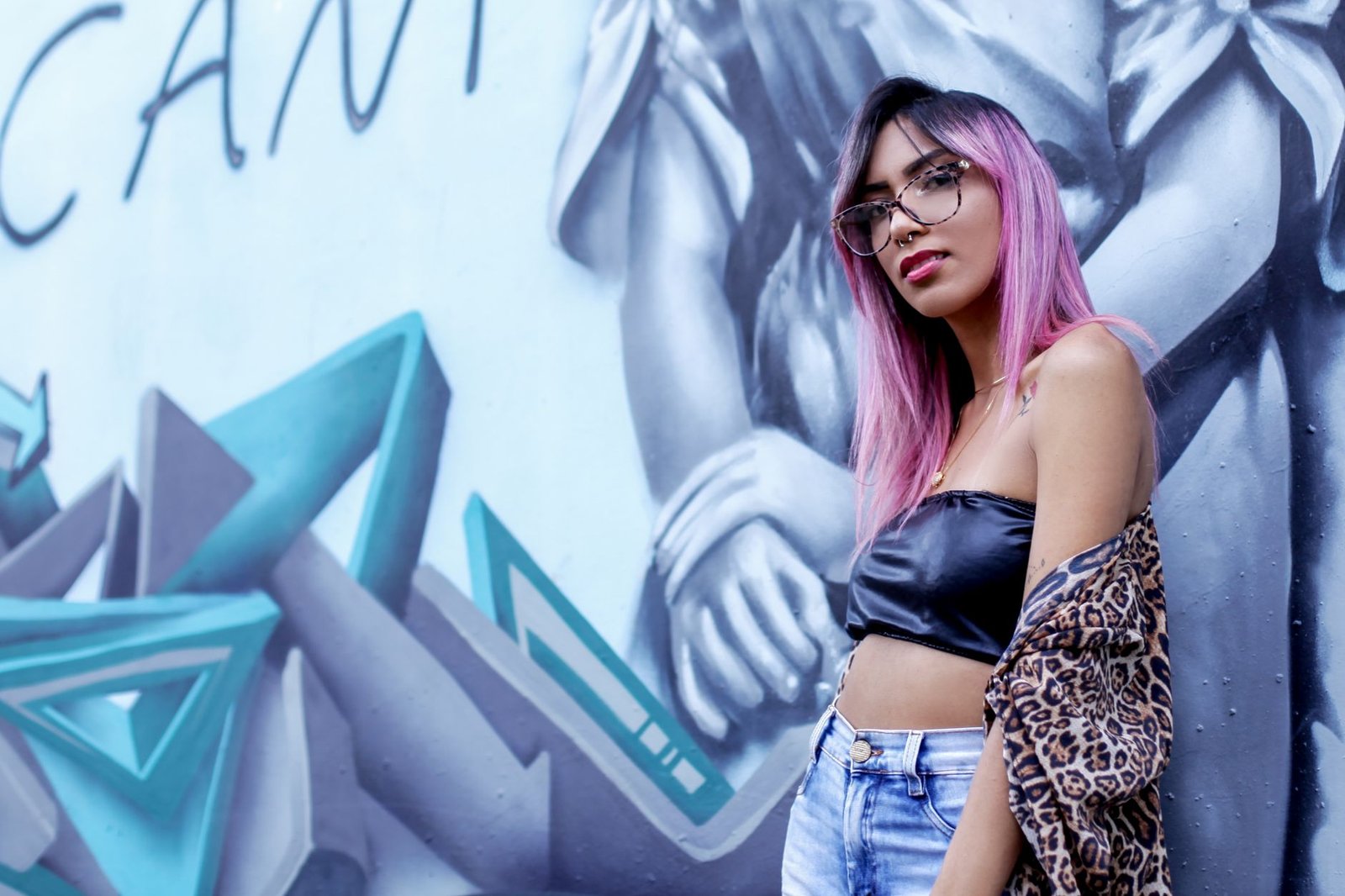 Stylish woman with pink hair poses against a graffiti backdrop.