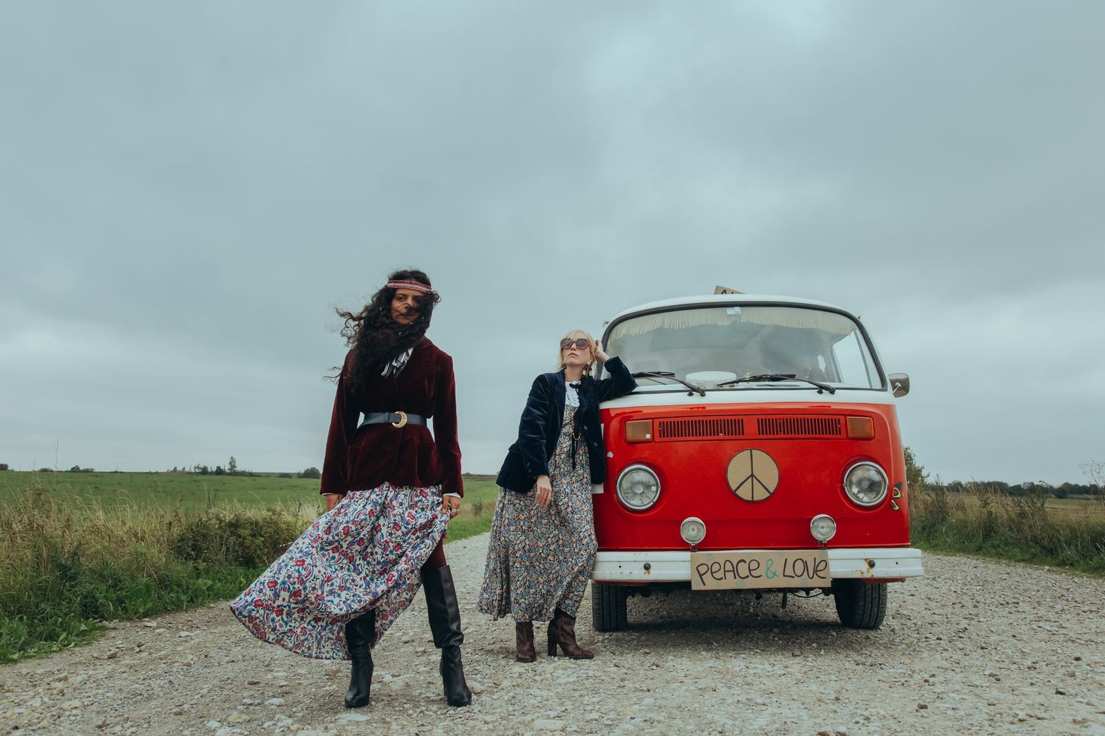 Two women in bohemian style outfits standing beside a vintage red van with peace symbols.