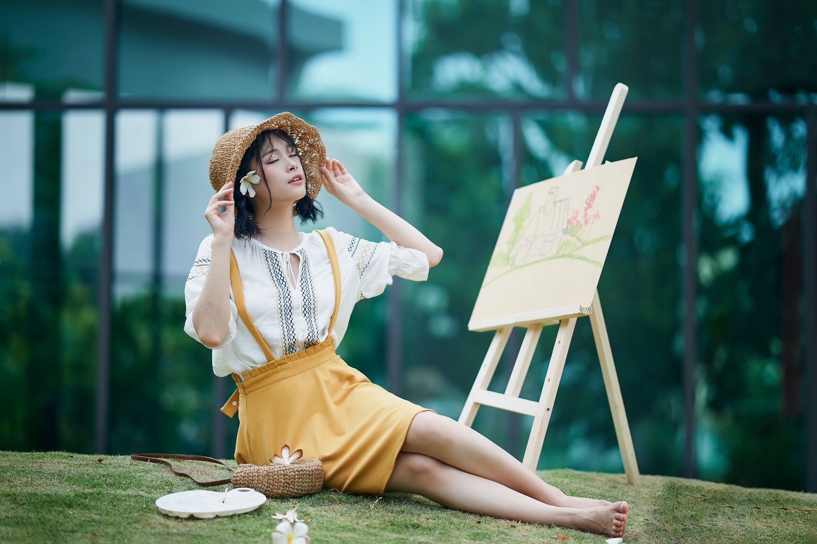 Asian woman in a sun hat relaxes with painting outdoors, embodying serenity and creativity.