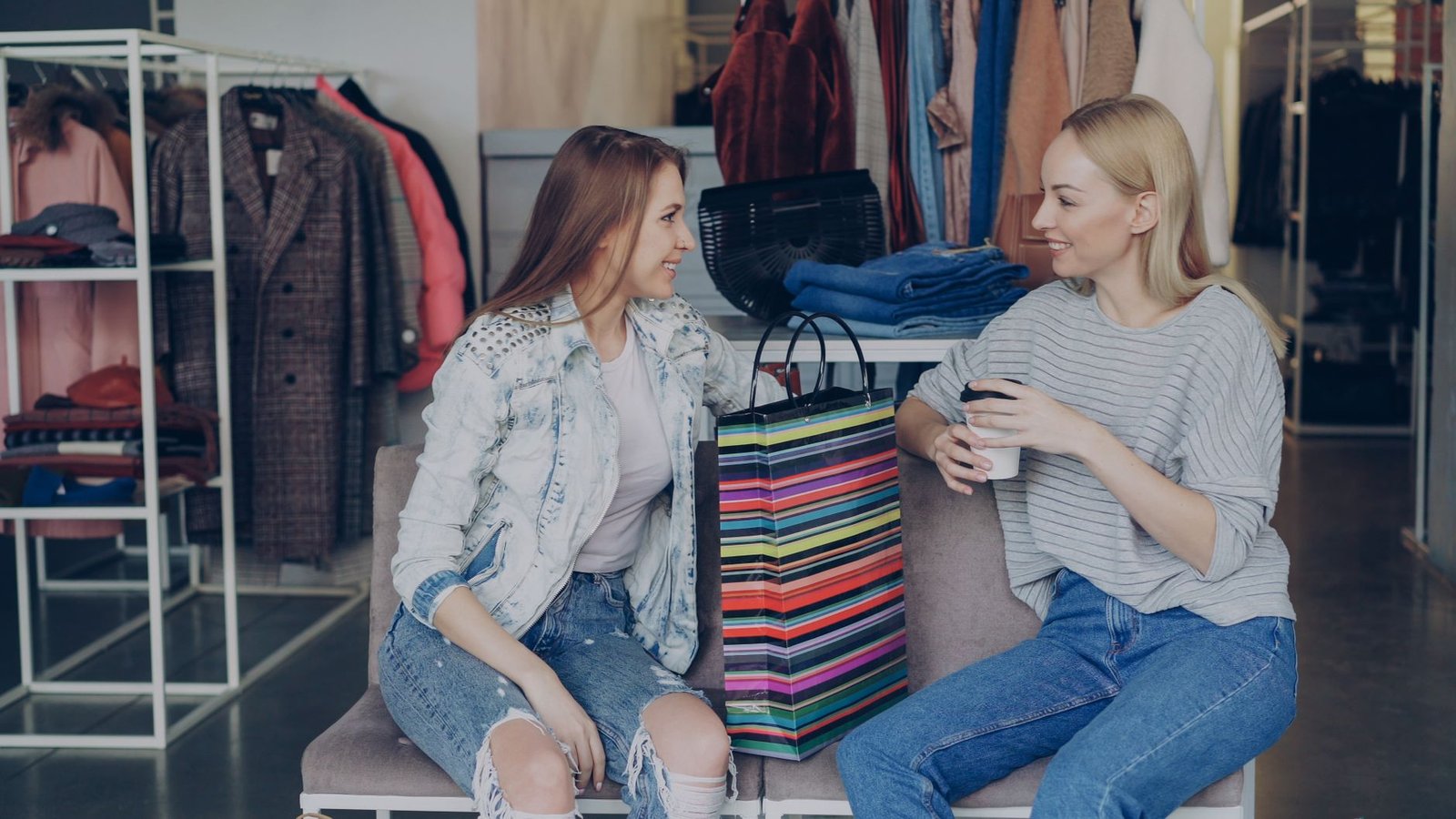 Two women enjoying a shopping break with colorful bags in a clothing store.