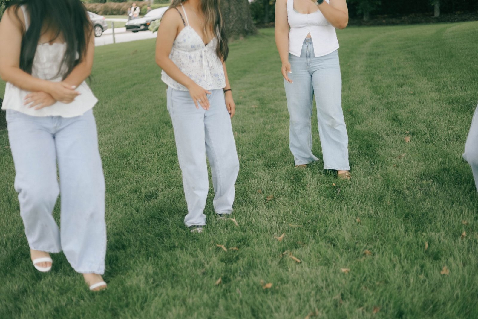 Three women in casual outfits chatting and having fun outdoors on a grassy lawn.