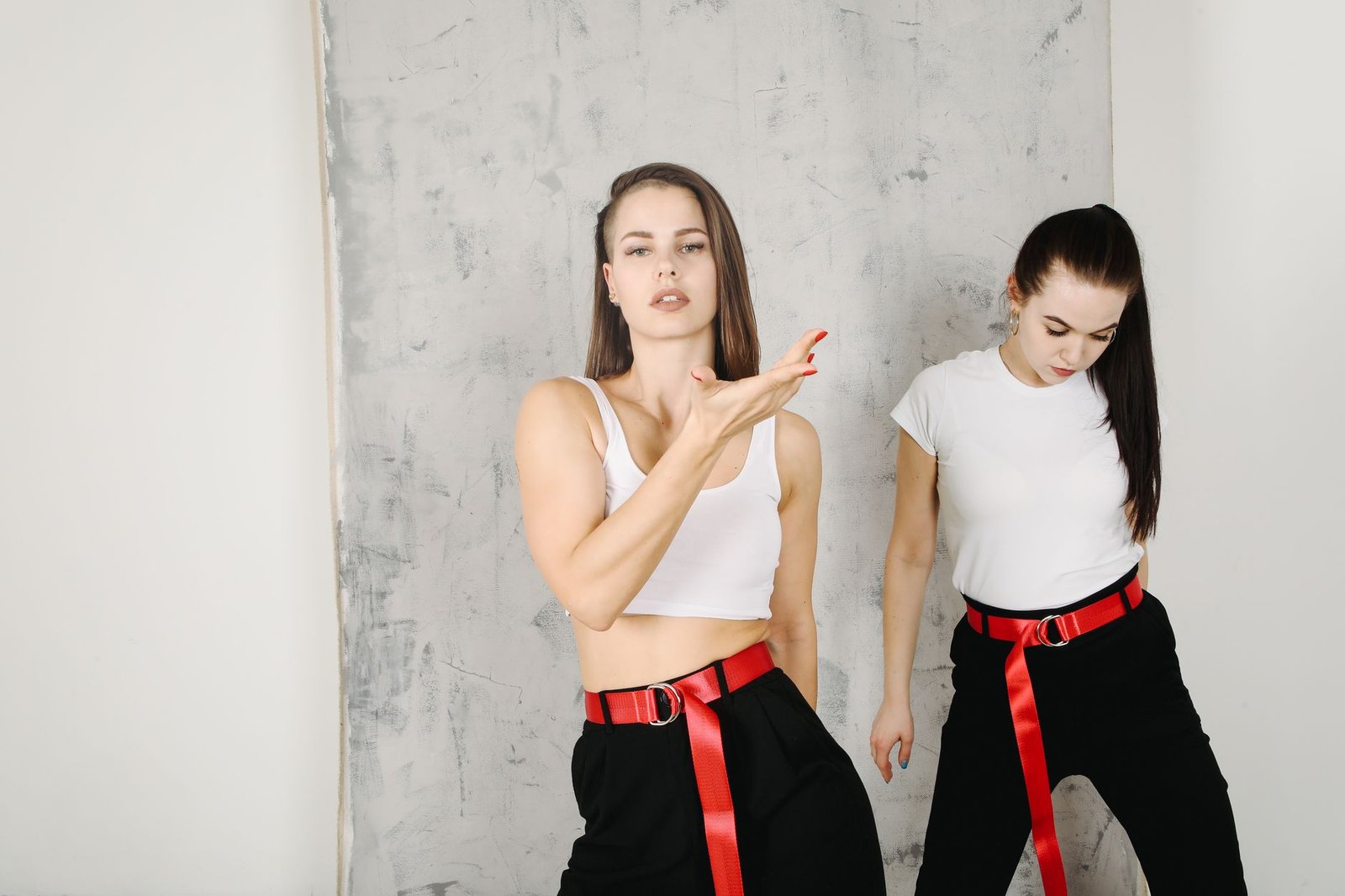 Two trendy women pose confidently against a minimalist background, showcasing modern style.