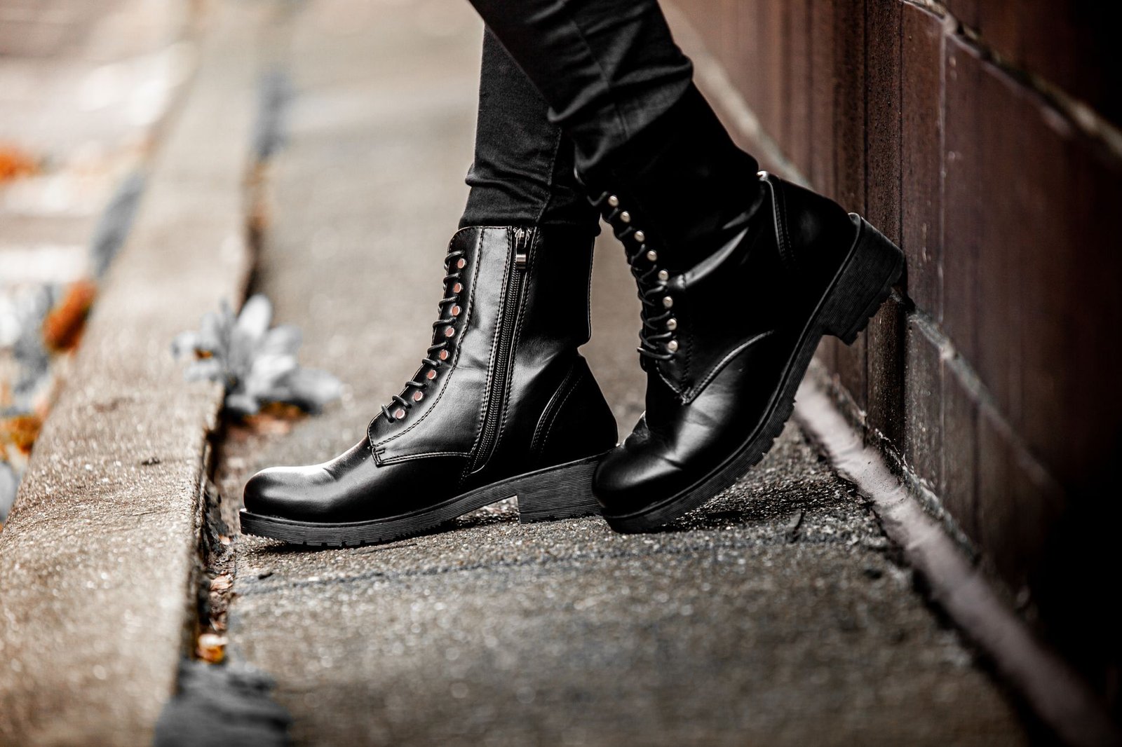 Black leather boots worn on a street sidewalk, displaying edgy fashion style.