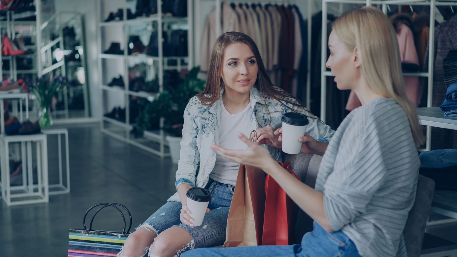 Two women talking and enjoying coffee while shopping in a stylish boutique.