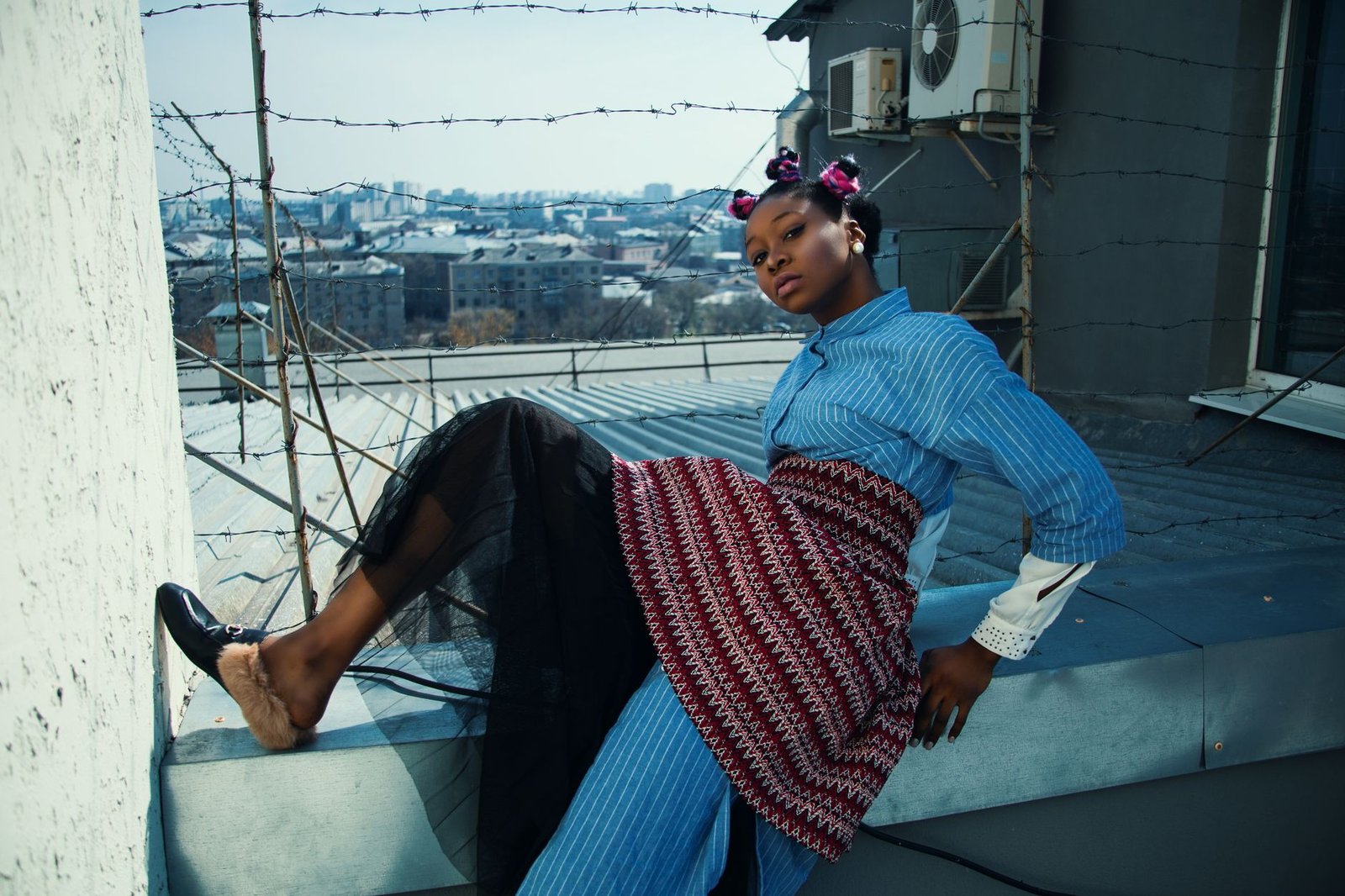 Stylish woman poses on a rooftop with urban landscape backdrop.