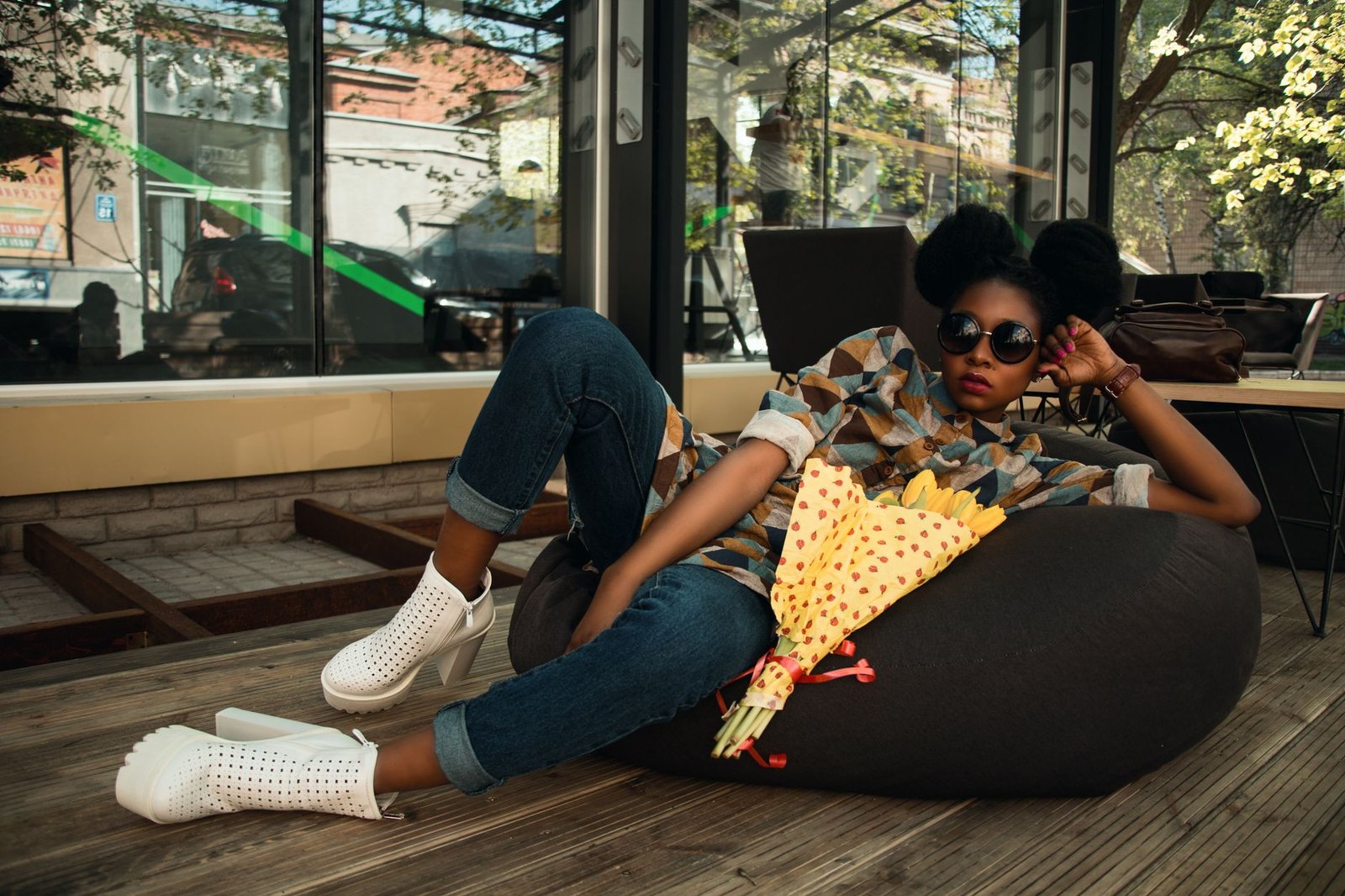 Young black woman in fashionable attire relaxing outside a café with flowers.