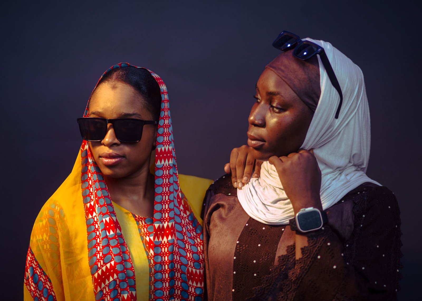 Two women in traditional African clothing, showcasing modern fashion with sunglasses and headscarves.