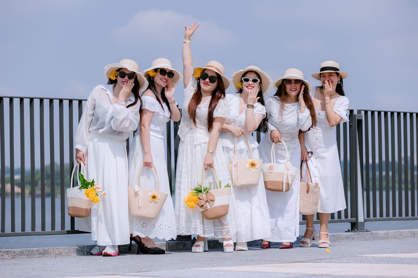 Group of women wearing white dresses and sun hats, posing outdoors with cheerful expressions.