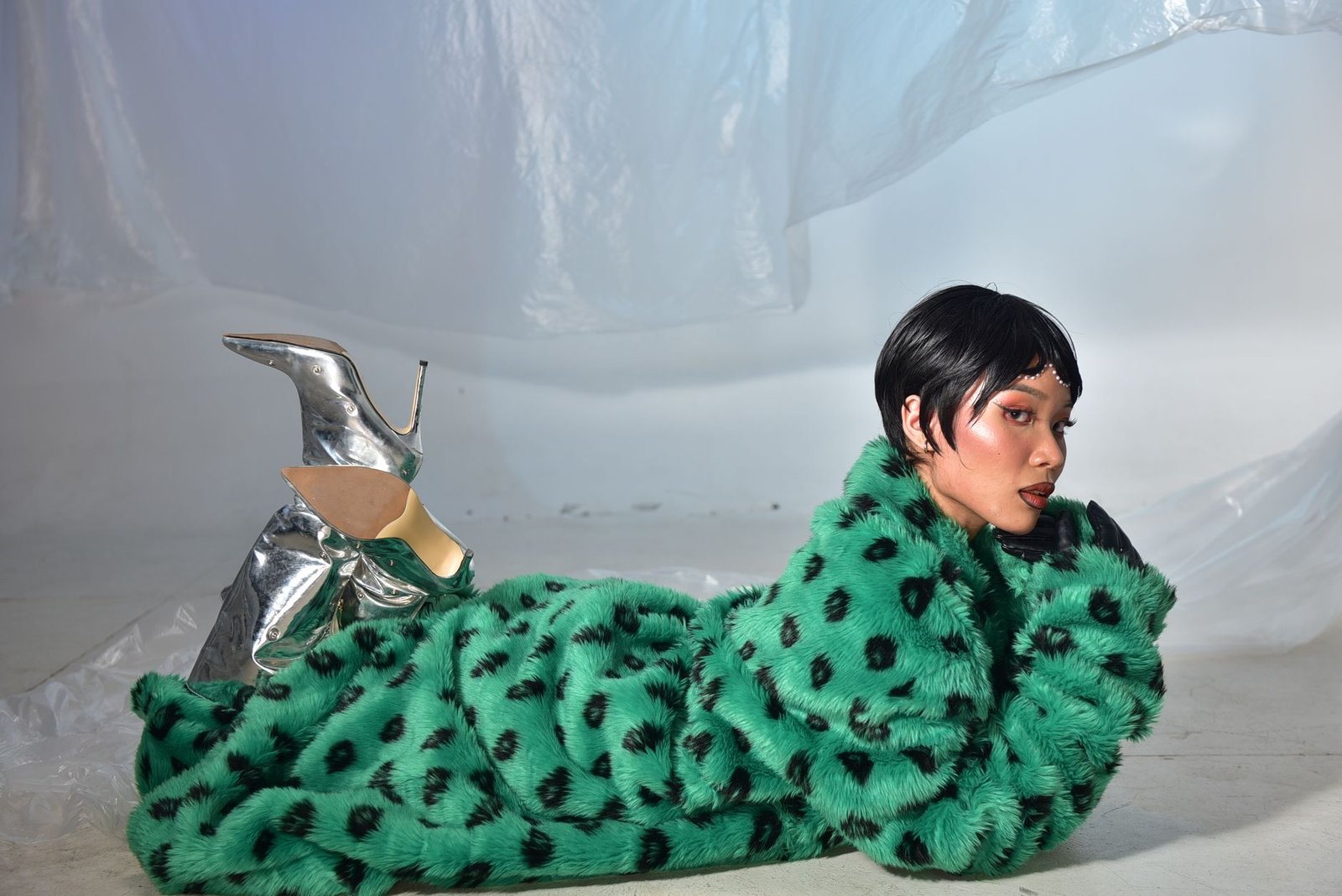 Trendy young woman in green faux fur coat and metallic boots striking a pose.