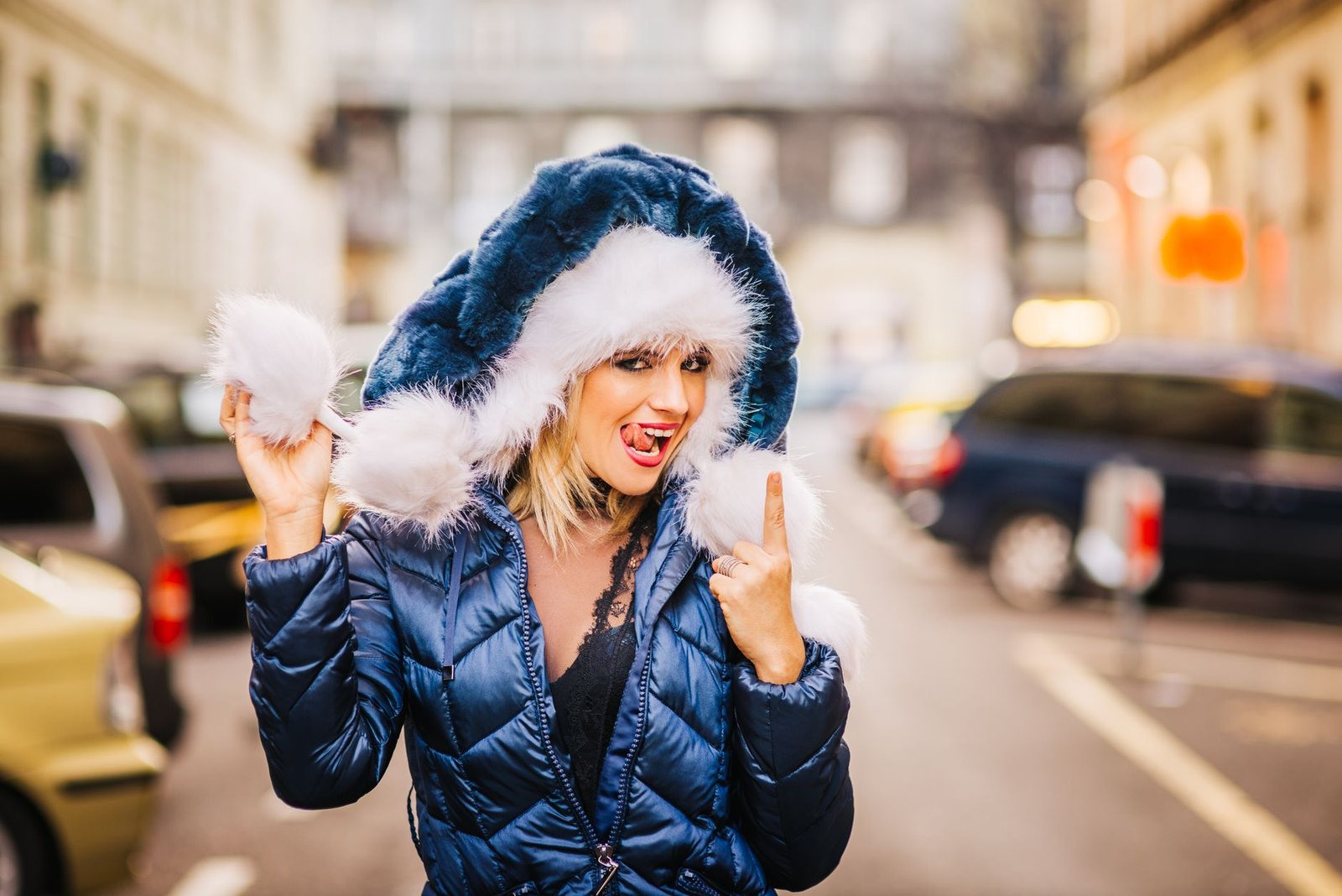 Smiling woman in blue coat and furry hat enjoying winter in an urban cityscape.