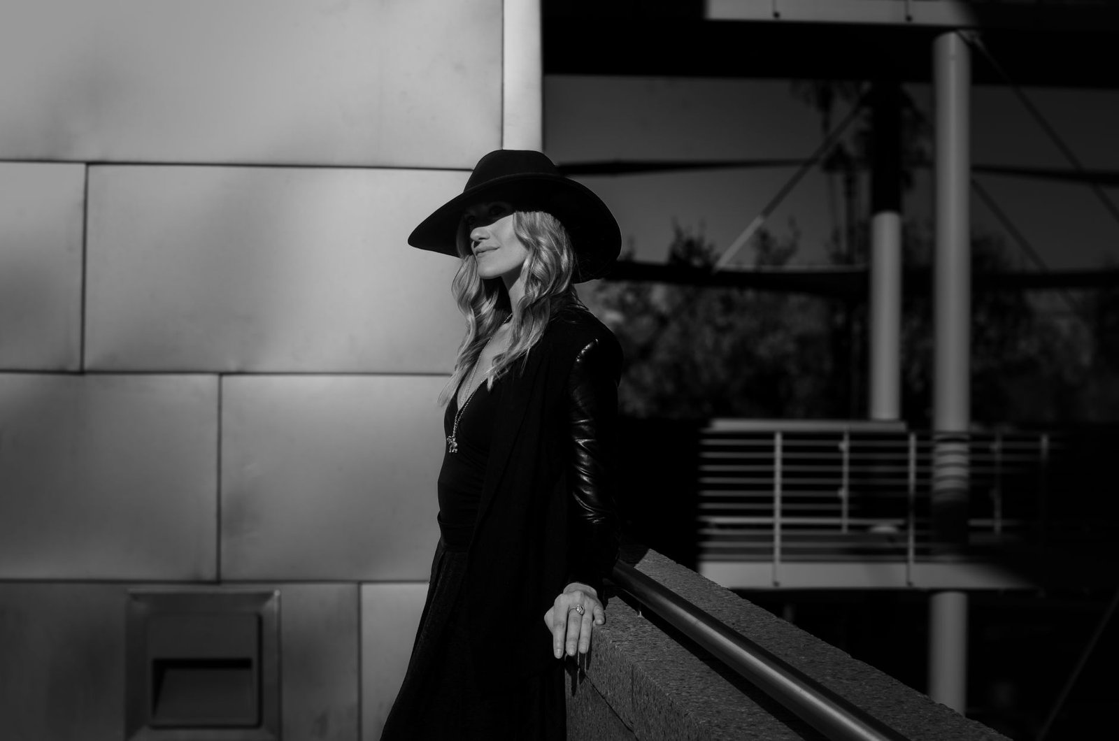Fashionable woman posing outdoors in black and white with a stylish hat and leather jacket.