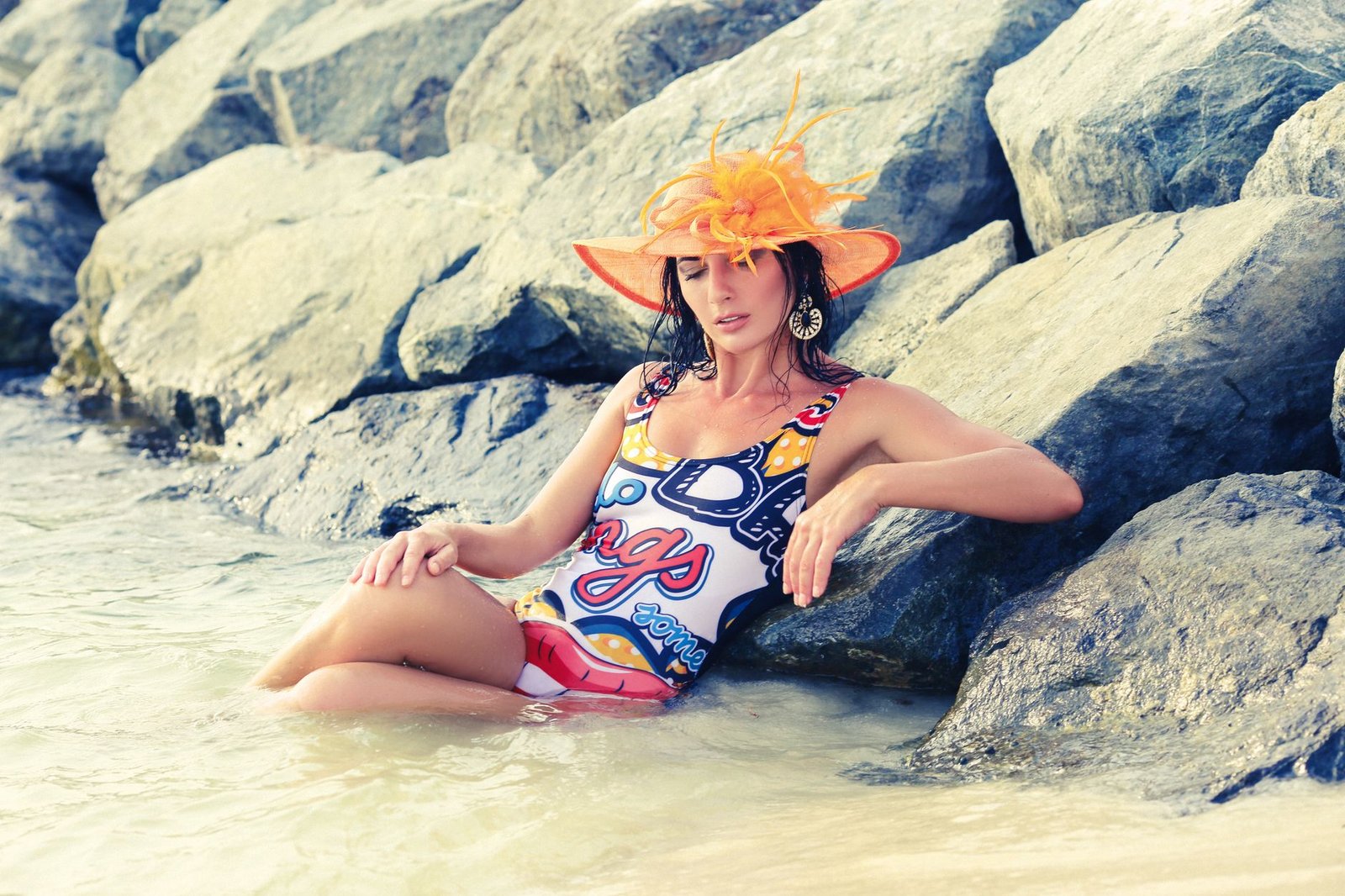 A fashionable woman in a vibrant swimsuit and hat relaxing by rocky shores in Dubai.