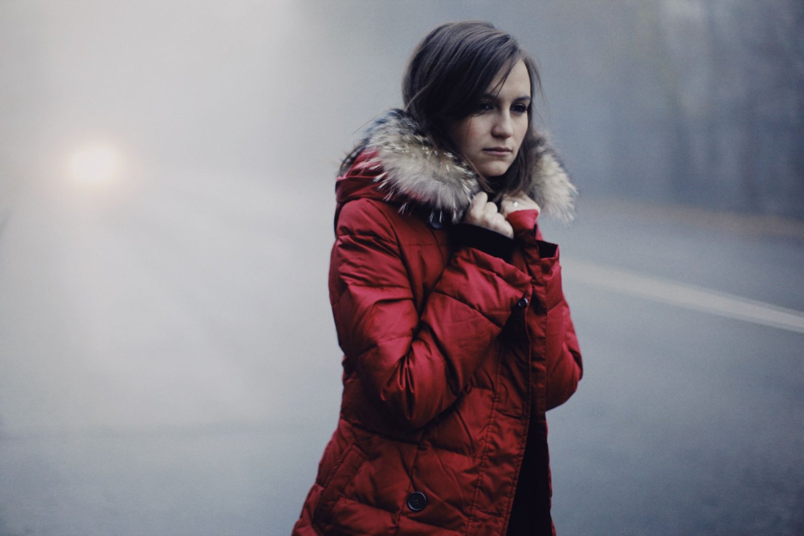 Young woman in a red winter coat walking on a foggy road.