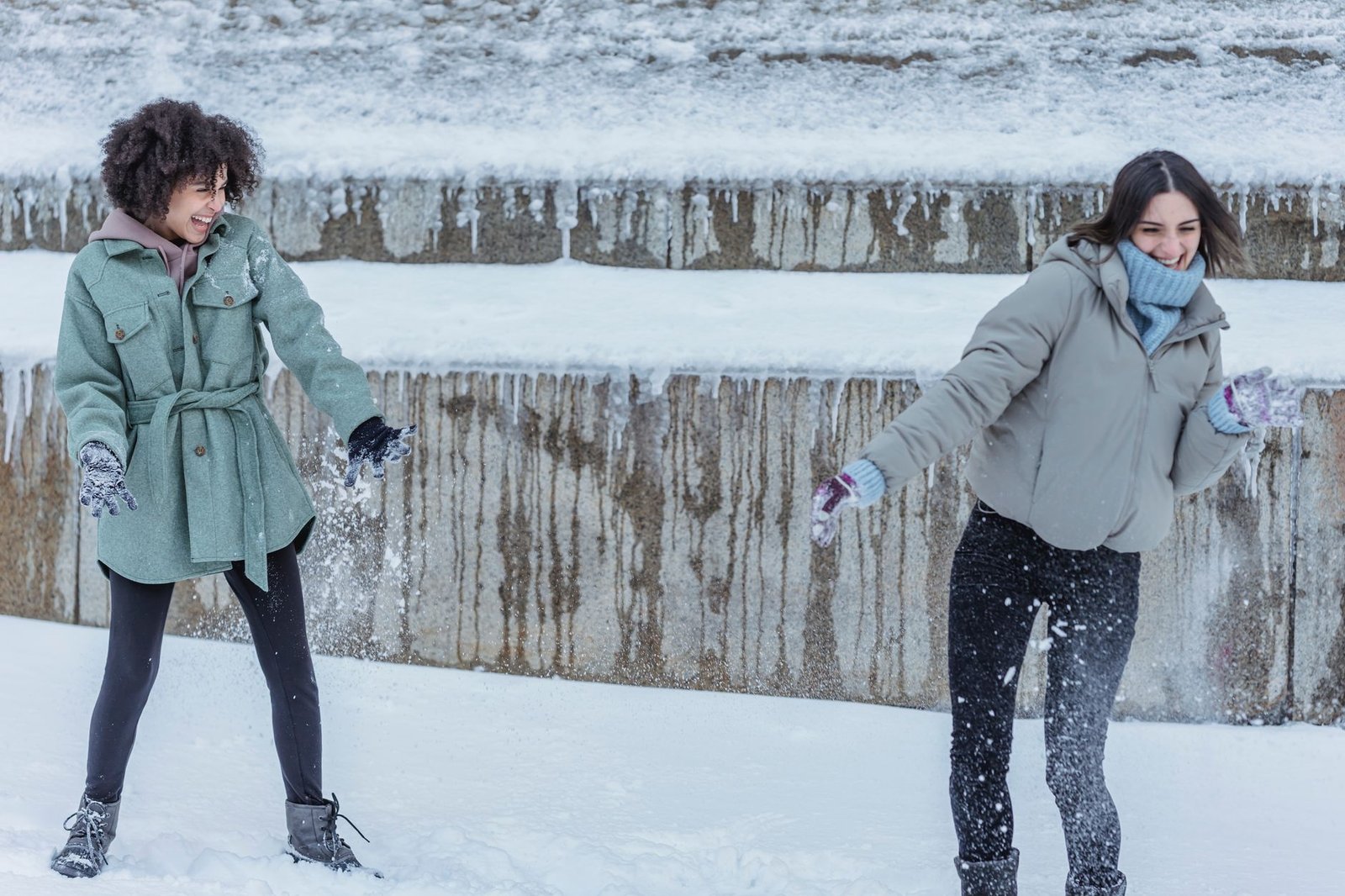 Delighted multiethnic girlfriends in outerwear laughing widely while having fun together in winter snowy park