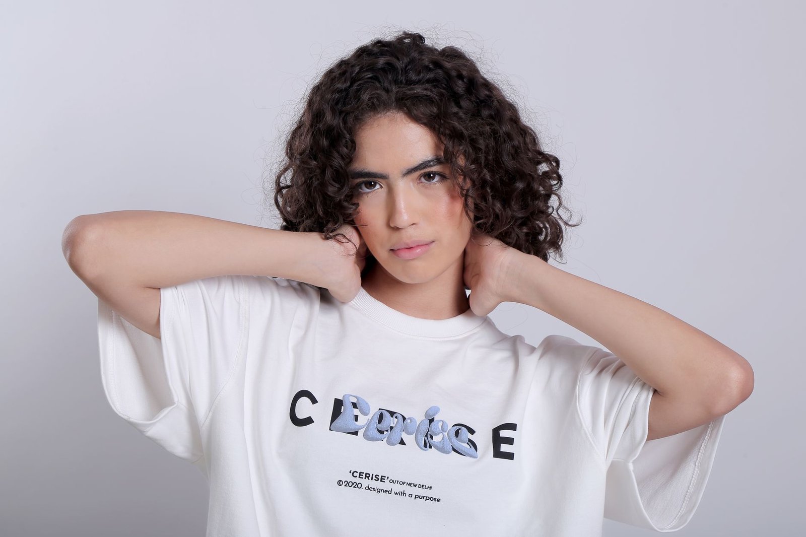 Woman with curly hair posing in a white t-shirt against a studio backdrop.