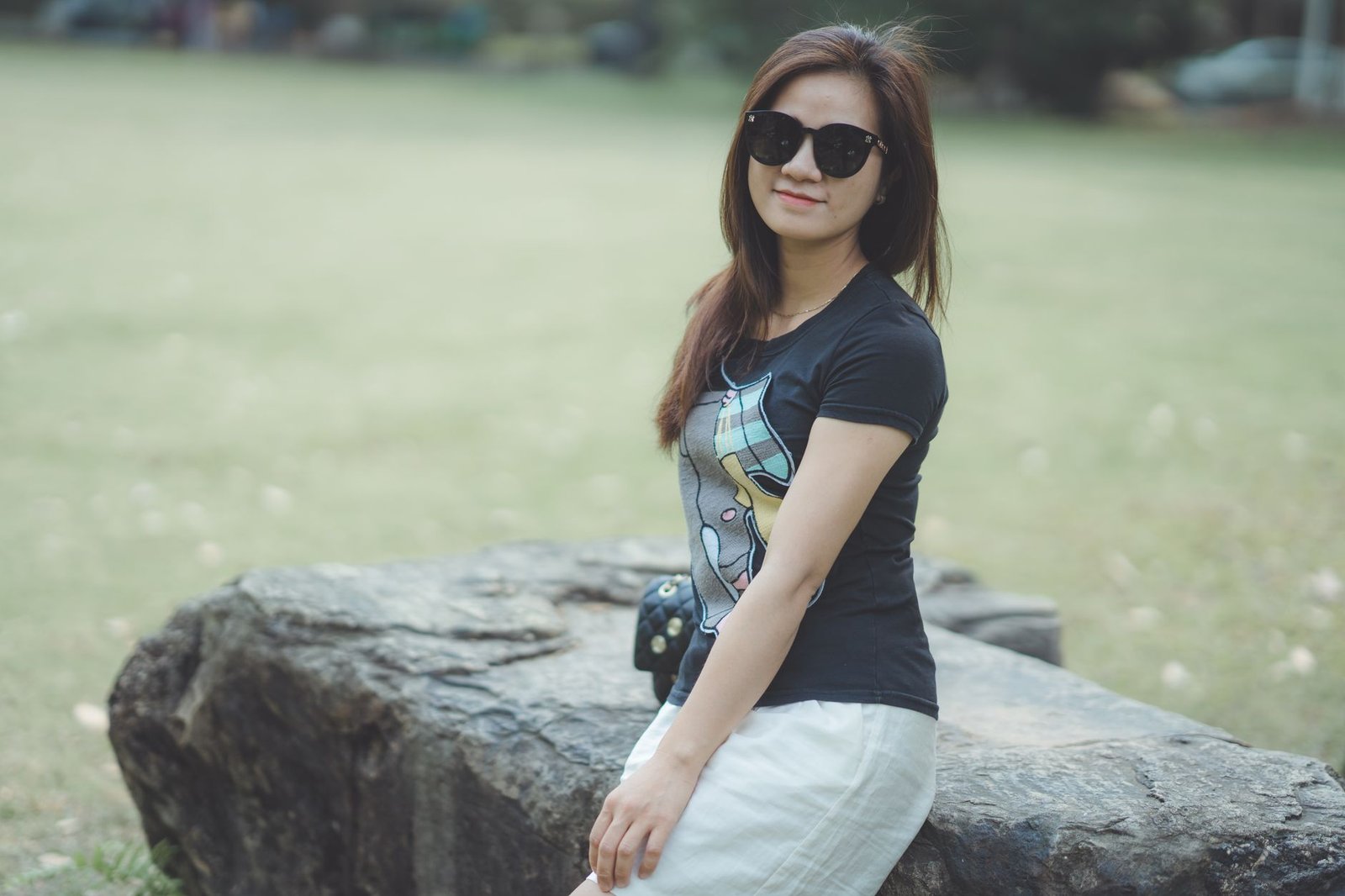 Casual portrait of a young woman sitting on a rock outdoors on a sunny day.