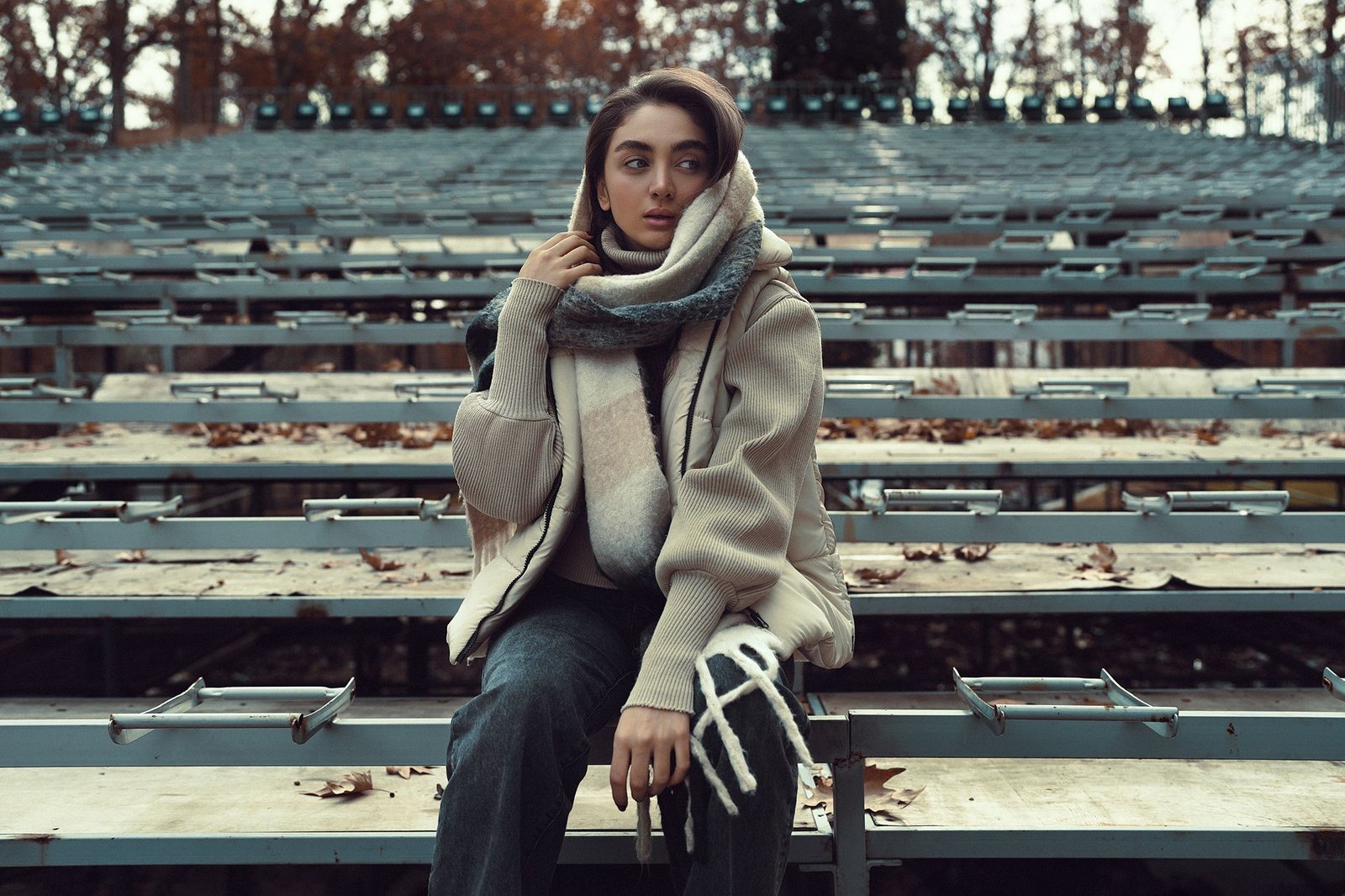 Stylish woman in fall attire on outdoor bleachers, serene autumn atmosphere.