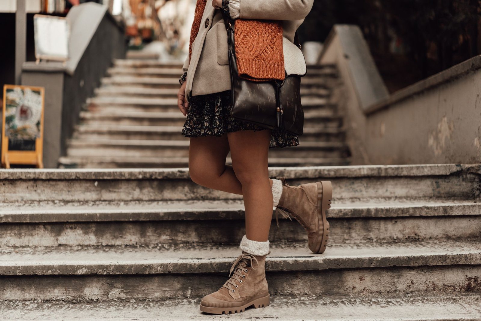 Faceless female in coat with scarf and short skirt bending leg while standing on snowy staircase in wintertime