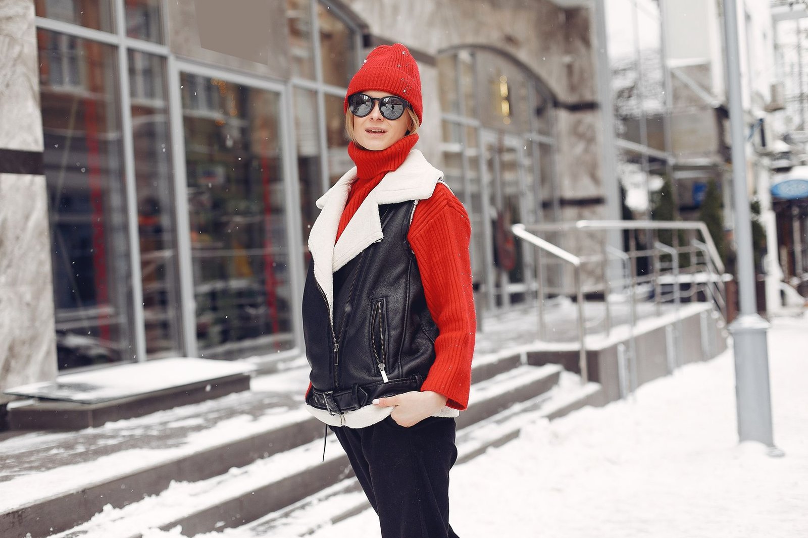 A fashionable woman in winter attire stands confidently on a snowy urban sidewalk.