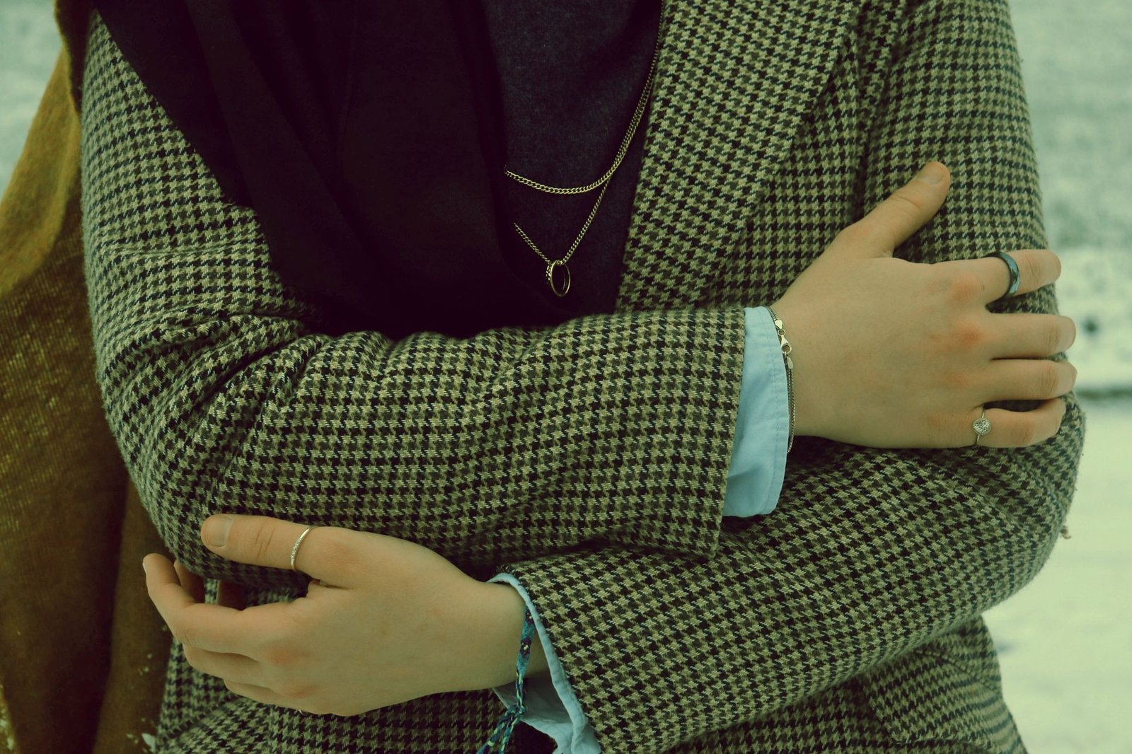 Fashion close-up of a woman in a houndstooth jacket with jewelry, emphasizing elegant style.