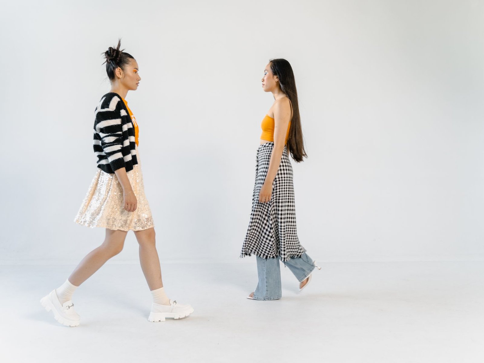 Stylish women in trendy outfits posing in a studio with a white background.