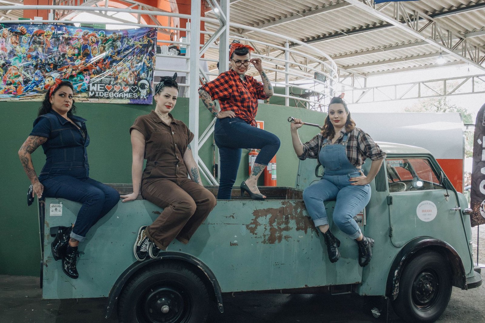 Stylish women in vintage attire posing on an old truck indoors.
