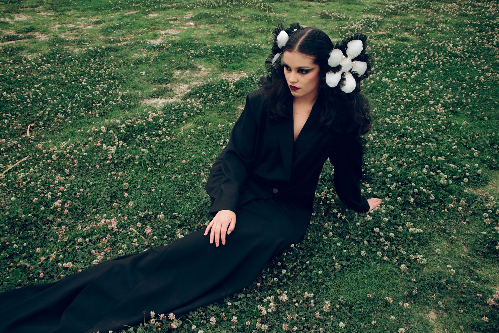 Stylish woman in black attire sitting elegantly on a lush green field with white flower accents.