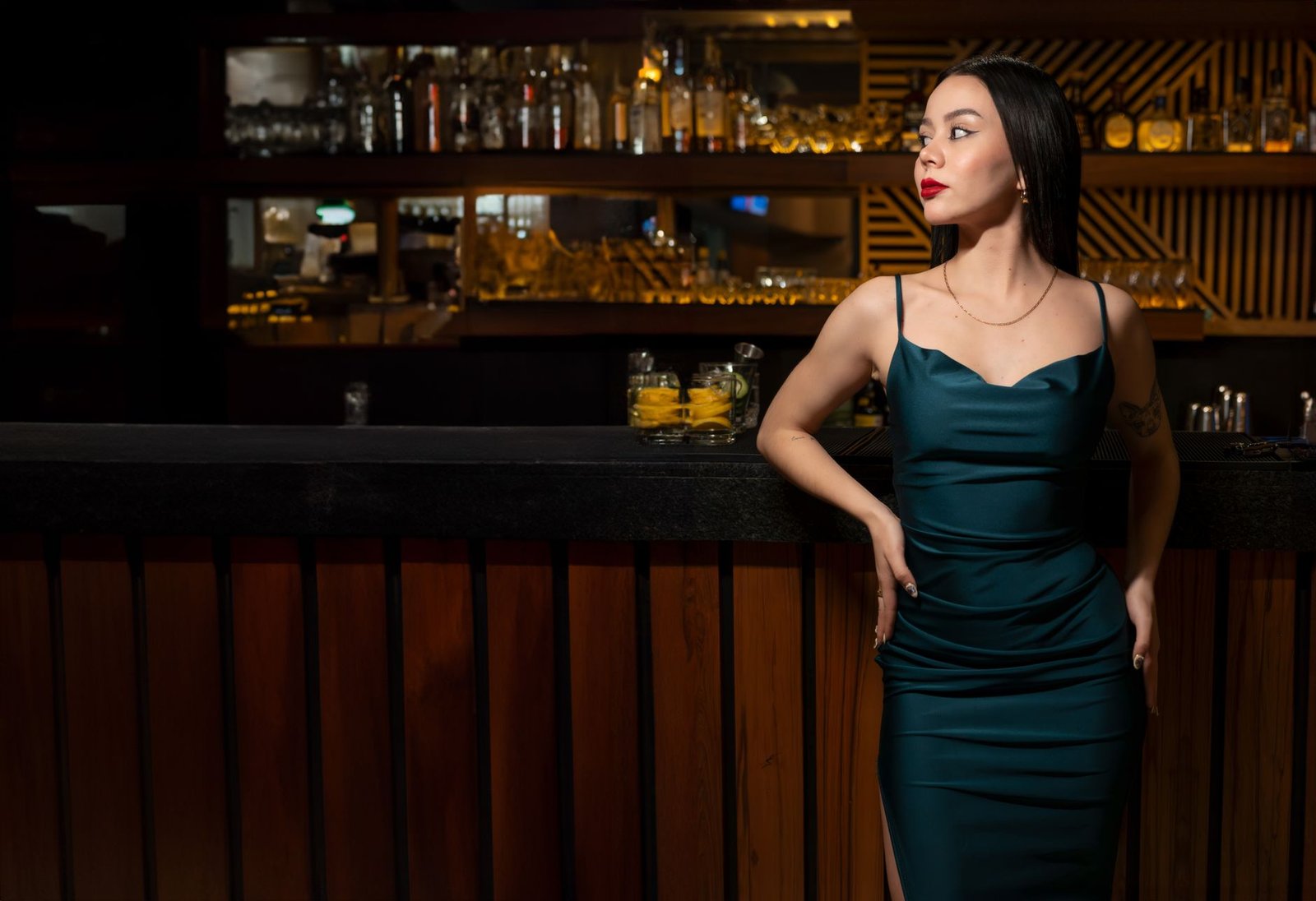 Portrait of a woman in a teal dress standing confidently at the bar, showcasing elegance and fashion.
