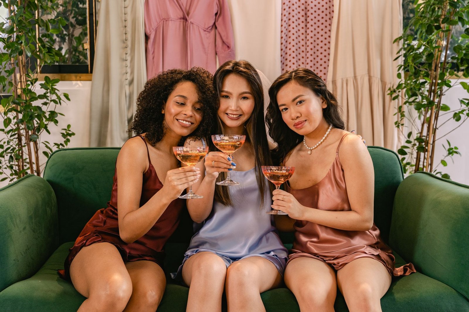 Three women enjoy a friendly gathering, toasting with wine in stylish loungewear on a sofa.