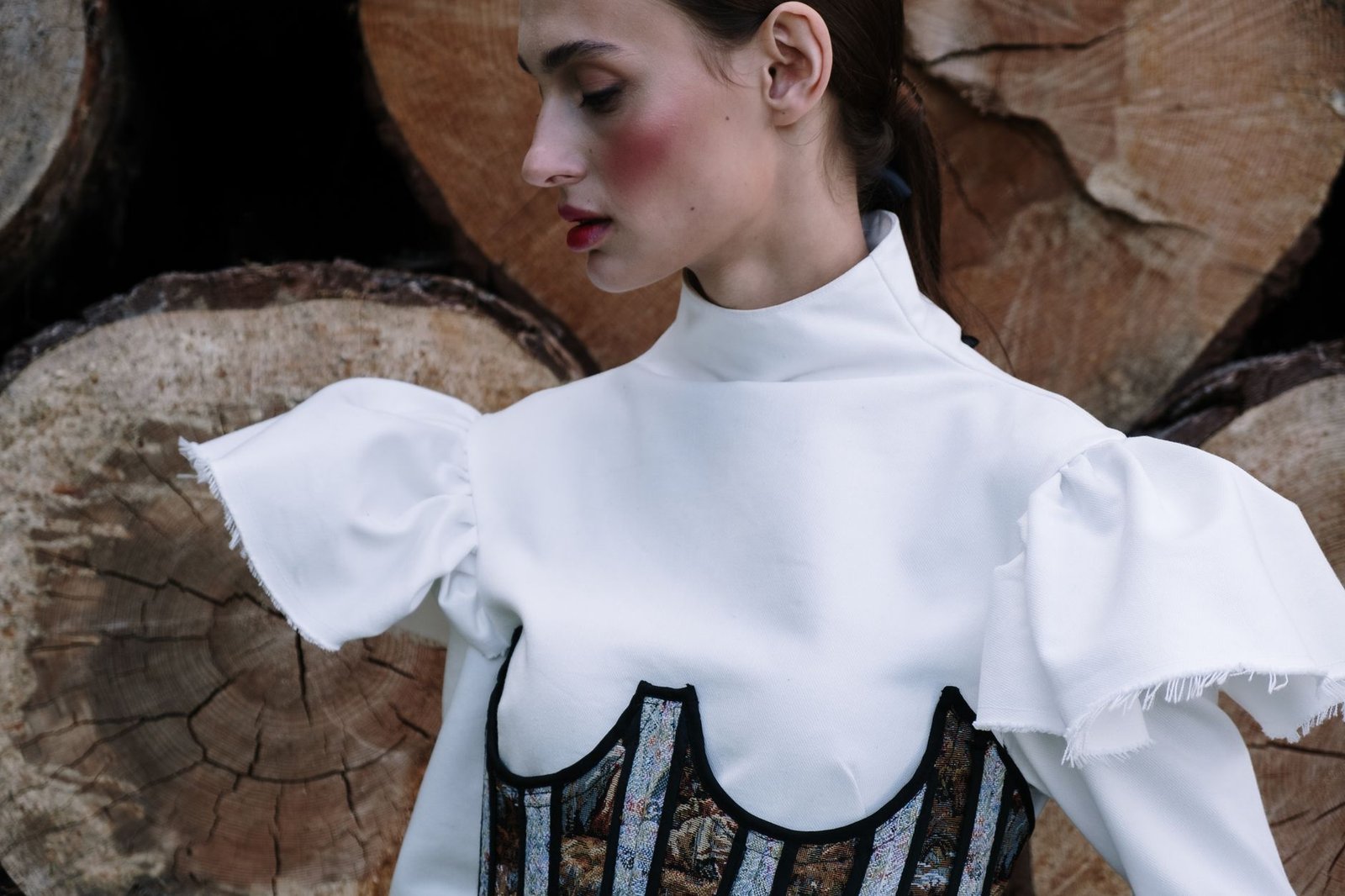 Portrait of a fashionable woman in a chic outfit posing outdoor with log backdrop.