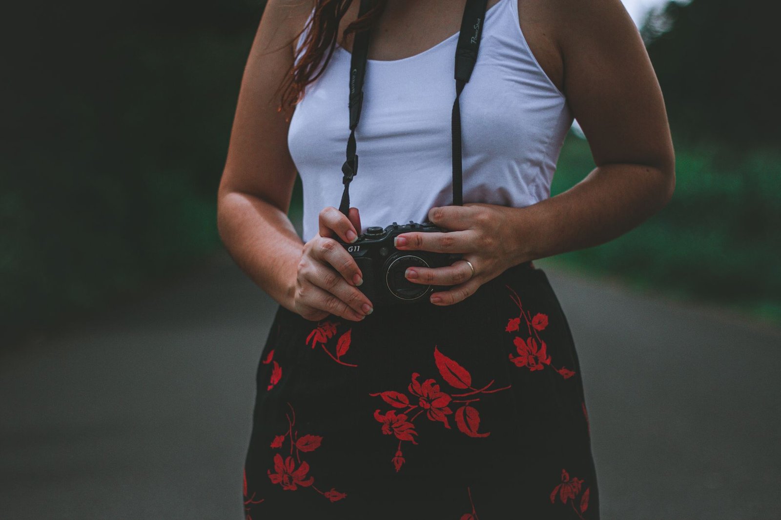Close-up of a woman holding a DSLR camera outdoors, wearing a white tank top.